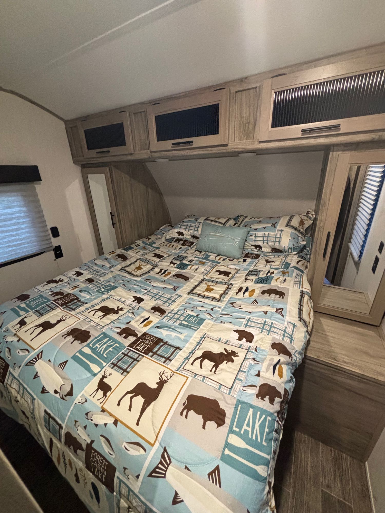 RV rental bedroom: a cozy retreat with nature-patterned bedding, overhead storage, and window blind.. Forest River Cherokee Alpha Wolf 2021