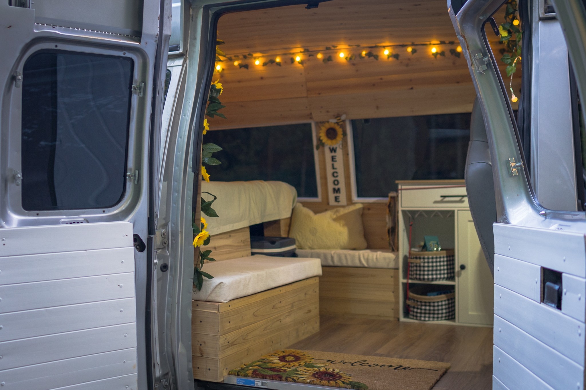 Step inside this cozy RV rental! Wood-paneled van interior with warm lights, comfy seating, and sunflower welcome decor.. Ford Econoline 2011