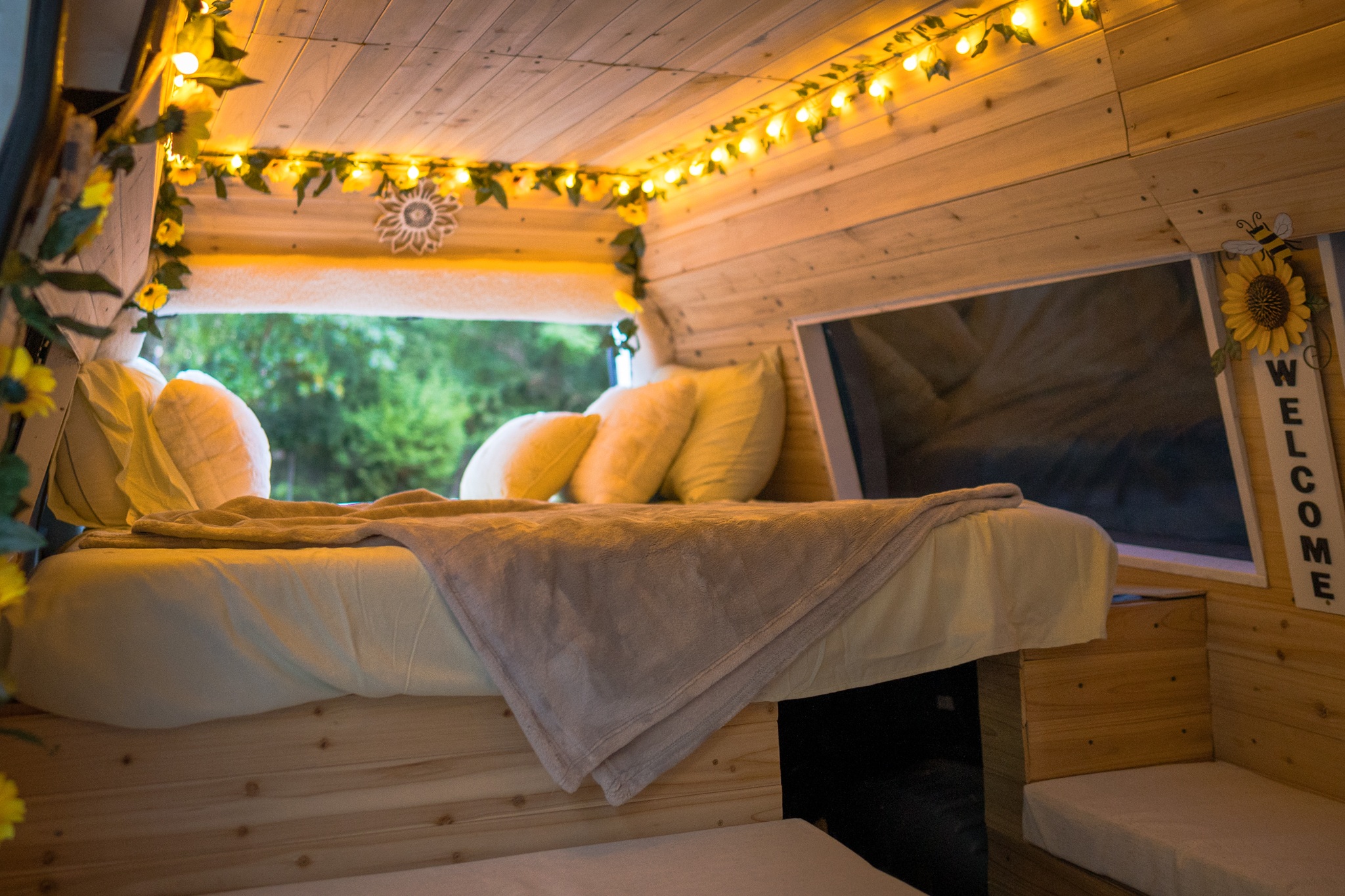 Cozy RV rental interior: bed, window view, and charming string lights on wooden walls create a welcoming retreat.. Ford Econoline 2011