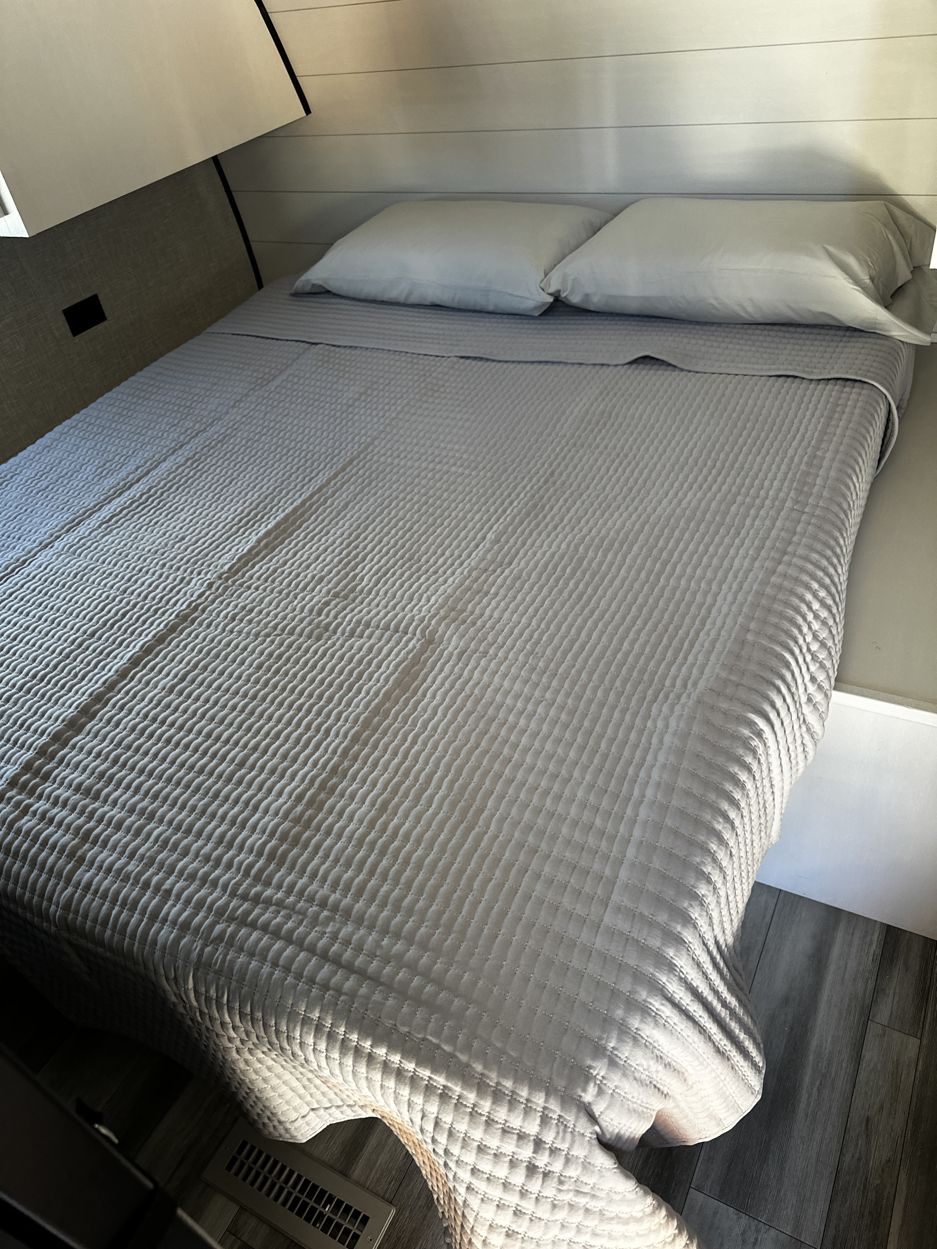 Cozy RV rental bedroom featuring a light grey quilted bedspread and white pillows, bathed in sunlight.. Starcraft Autumn Ridge 2024