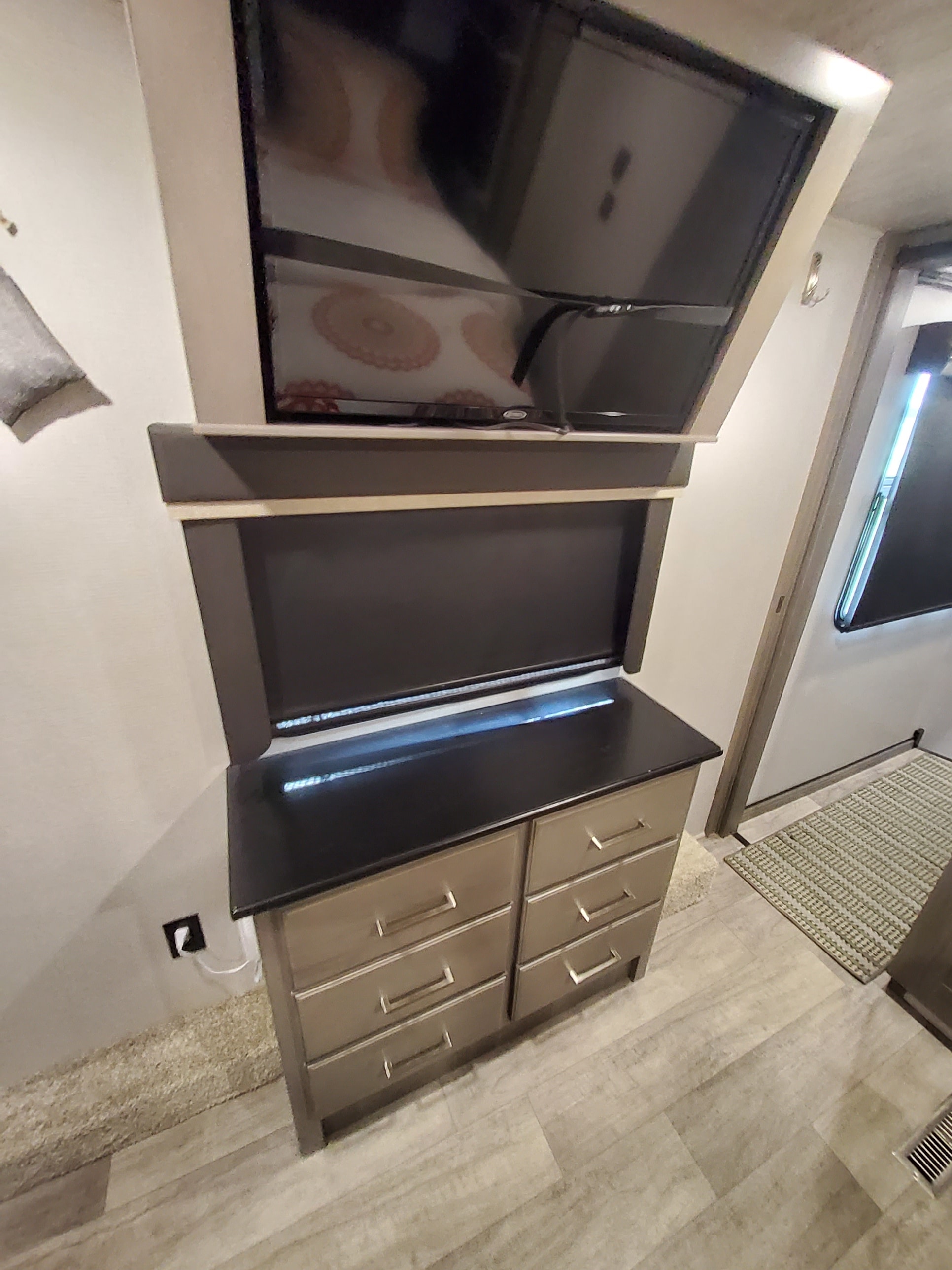 RV rental bedroom interior with a wall-mounted TV, built-in dresser with six drawers, and light wood-look flooring.. Keystone RV Montana 2021