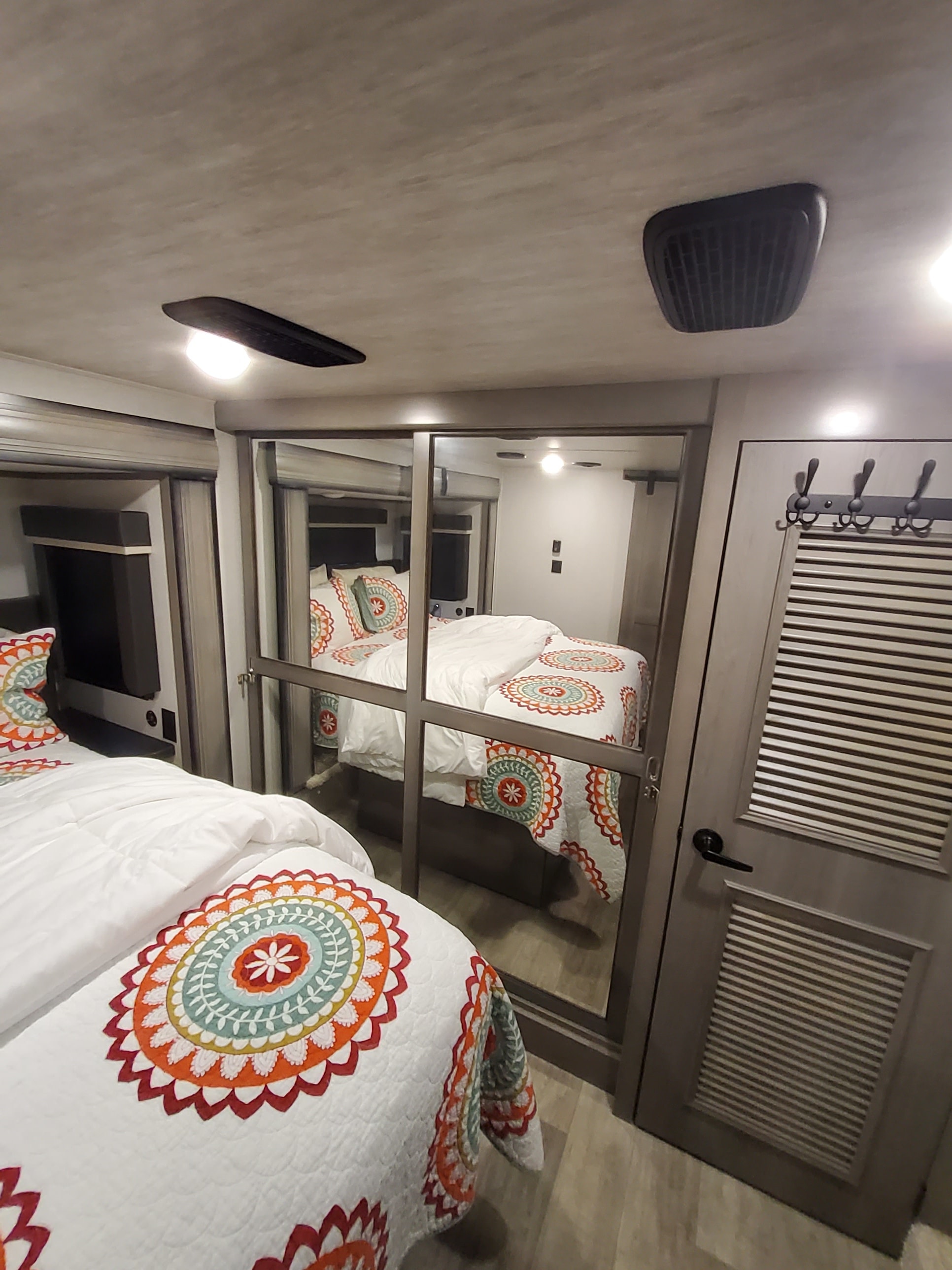 RV rental bedroom showcasing vibrant mandala-patterned bedding, mirrored wardrobe doors, and handy wall hooks.. Keystone RV Montana 2021