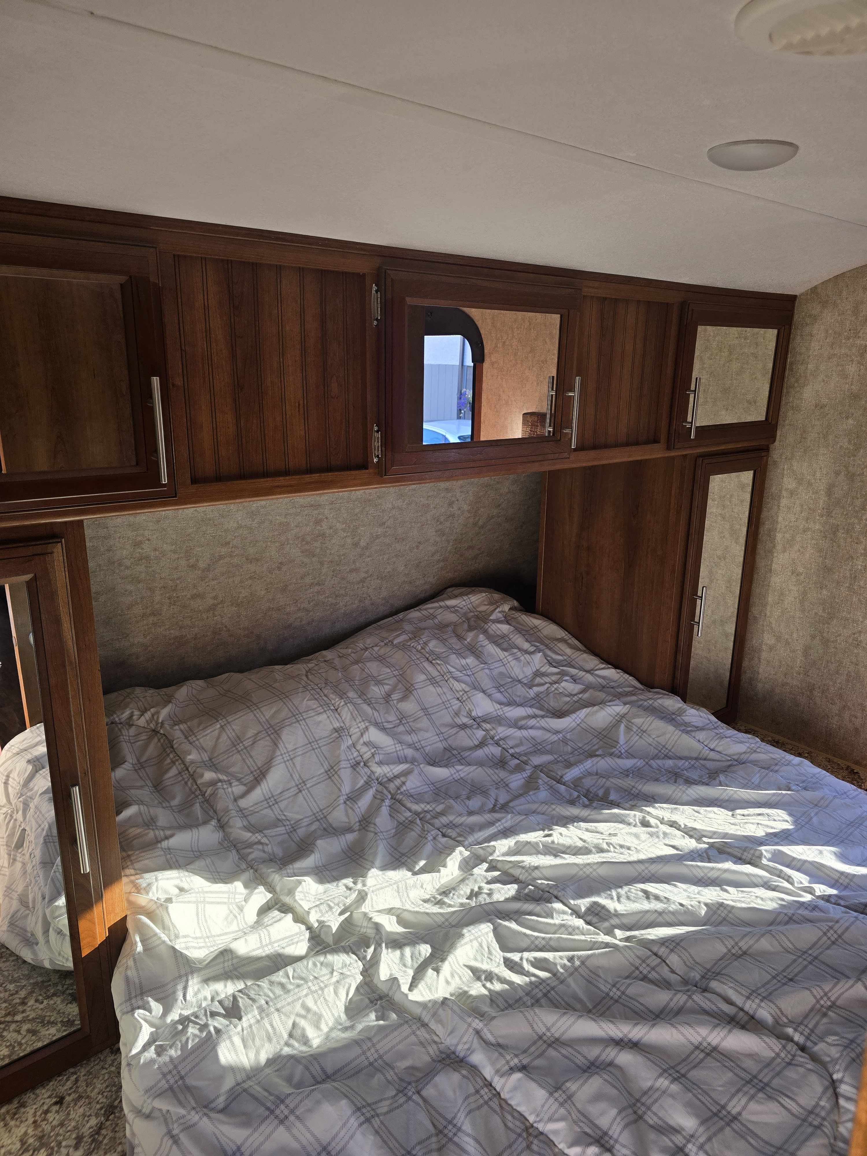 Cozy RV rental bedroom featuring a comfy bed with plaid comforter, wood cabinets, and warm sunlight.. Forest River Tracer Air 2017