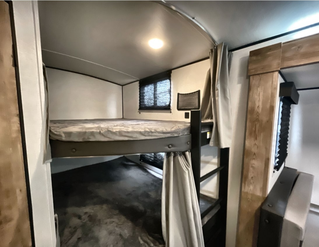 Inside an RV rental: a cozy sleeping area featuring comfortable bunk beds with privacy curtains.. Keystone RV Springdale 2021