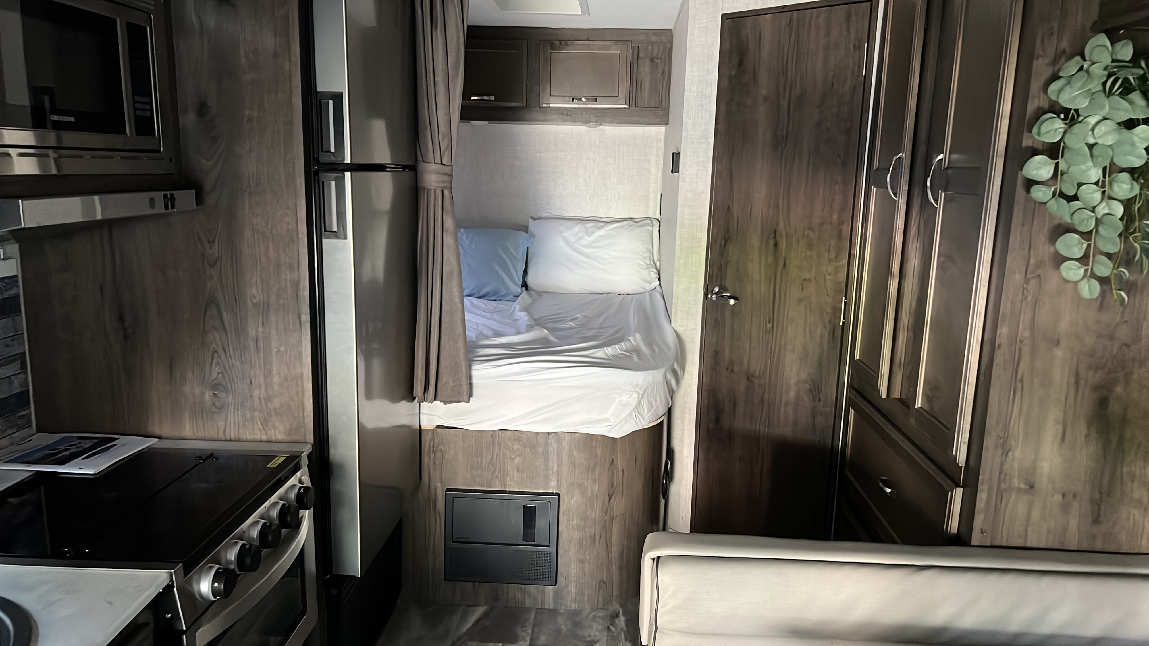 RV rental interior: a compact kitchen with stove & microwave, a cozy bed, fridge, and wood-paneled storage solutions.. Gulf Stream Conquest 2022