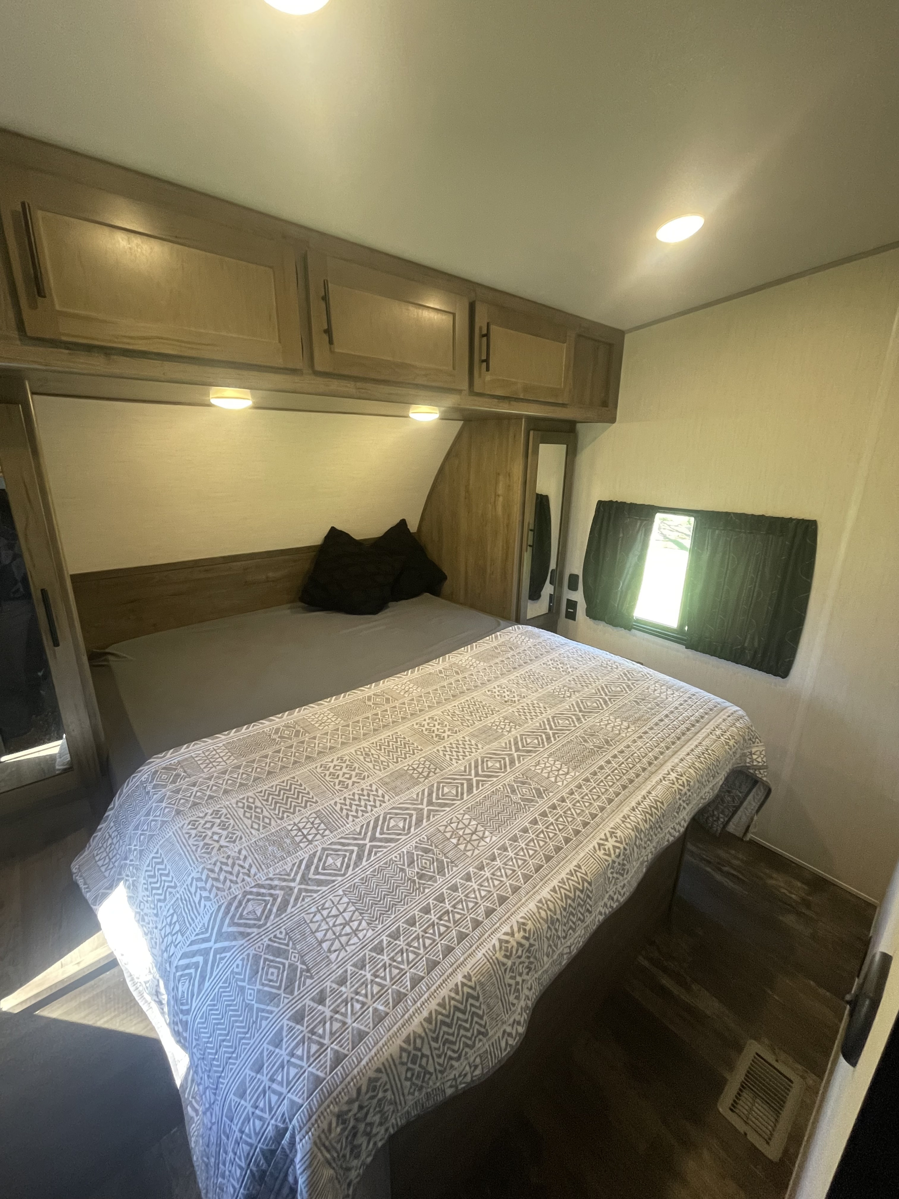 RV rental interior: cozy bedroom with a patterned bedspread, wood cabinets, and bright window.. Forest River Cherokee Wolf Pack Toy Hauler 2021
