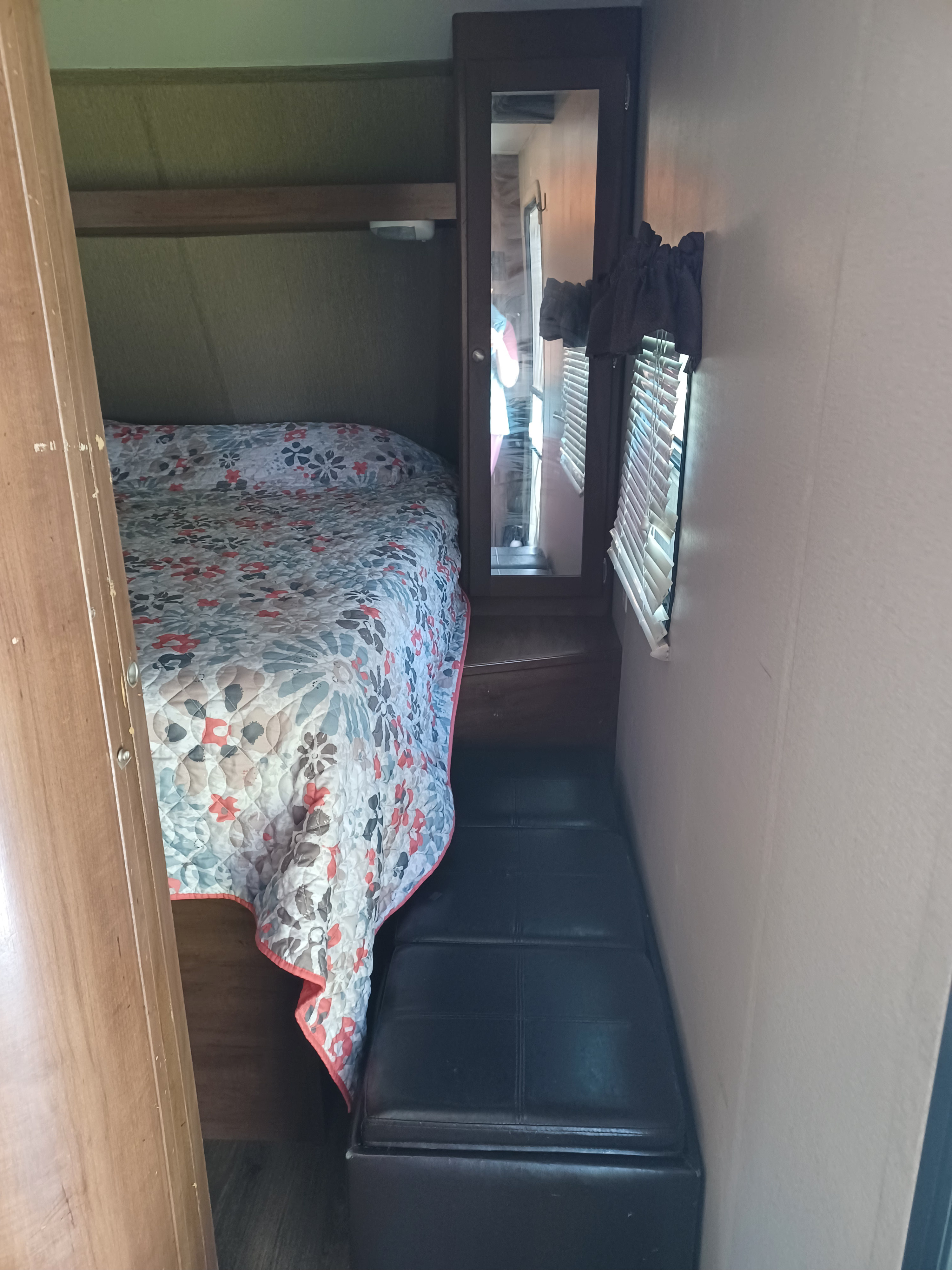 RV rental sleeping area: bed with floral quilt, mirrored storage, window, and a dark ottoman. Compact interior.. Aspen Trail Aspen Trail Trailer 2015