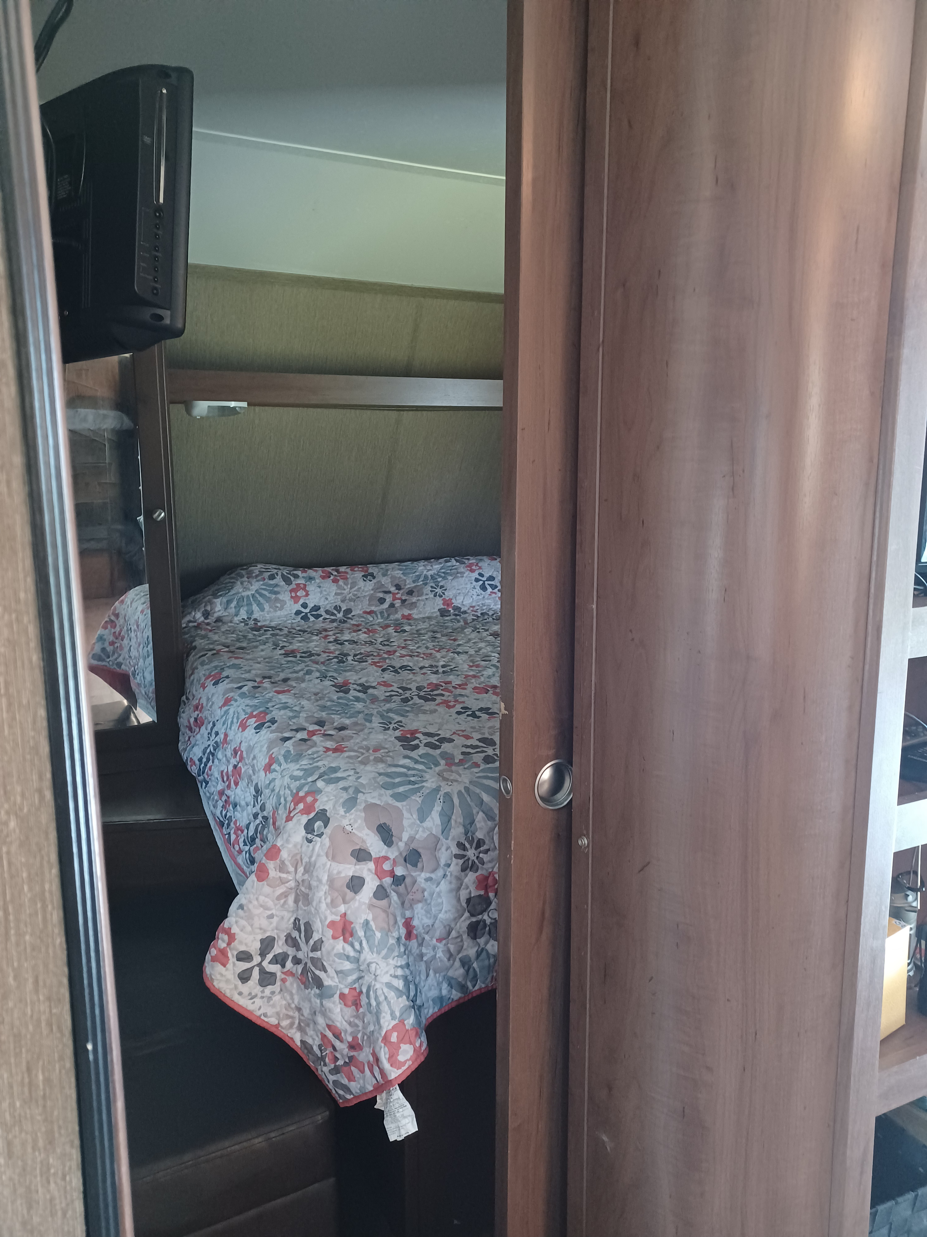 Cozy RV rental bedroom featuring a bed with a floral quilt, steps, and a wall-mounted TV, ideal for compact living.. Aspen Trail Aspen Trail Trailer 2015