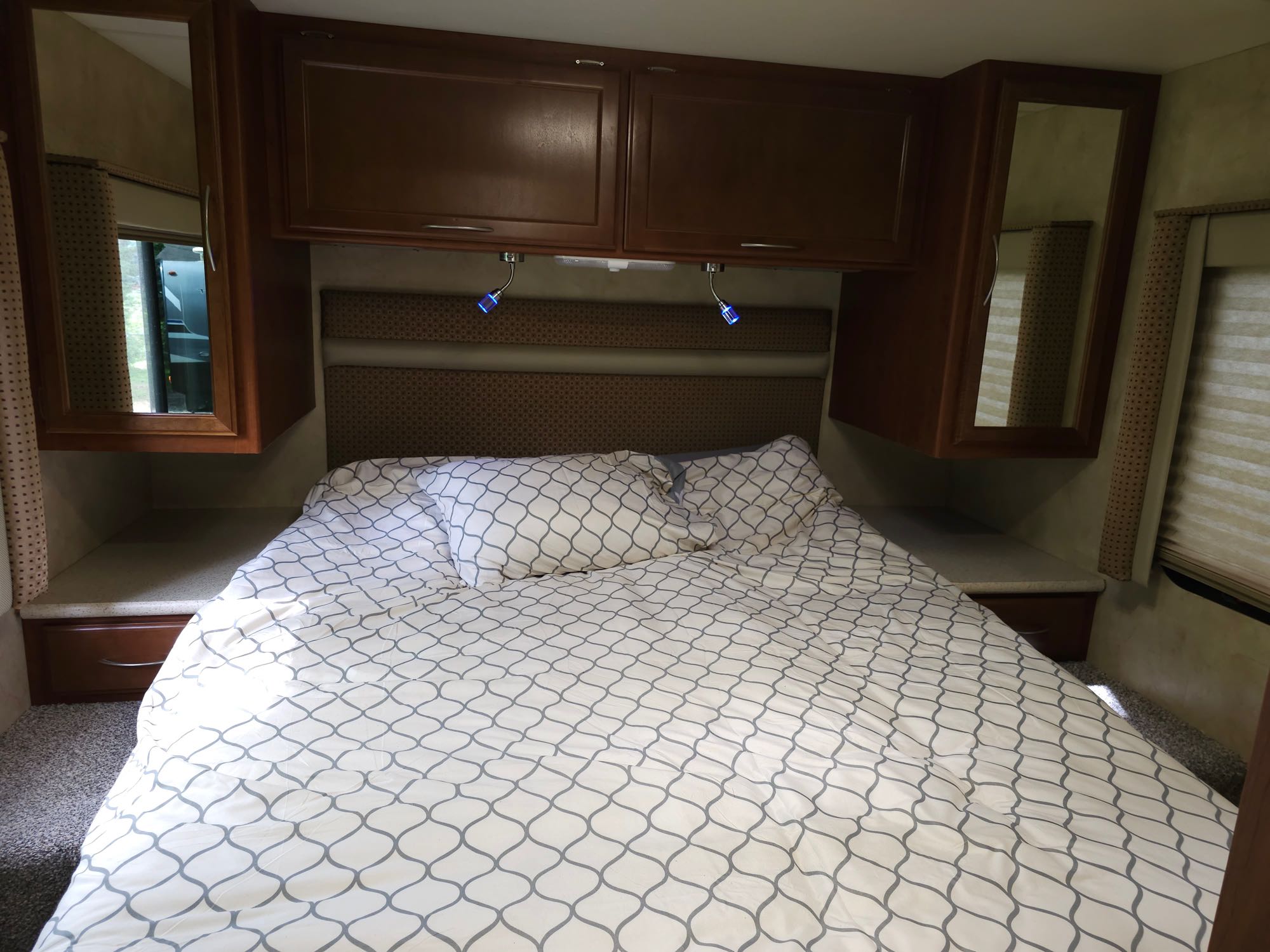 Cozy RV rental bedroom with white & grey patterned bedding, dark wood overhead cabinets, and reading lights.. Thor 29.1 2012