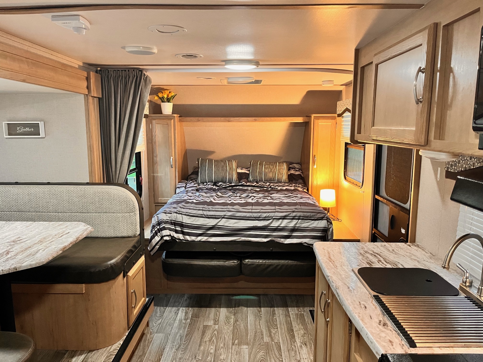 Cozy rv rental interior featuring a compact bedroom with striped bedding, a dinette, and a functional kitchen.. Winnebago Micro Minnie 2020