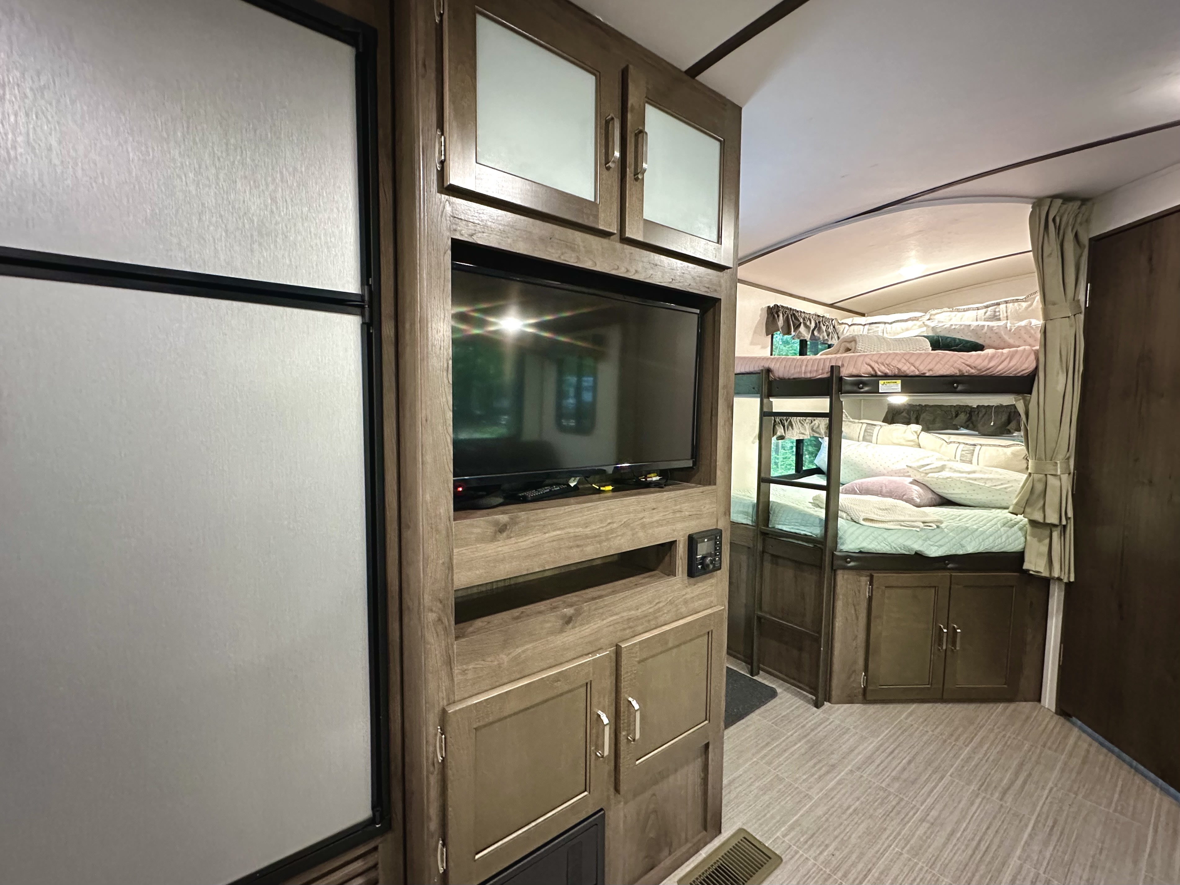 Spacious RV rental interior featuring a TV entertainment unit, refrigerator, and comfortable bunk beds with colorful bedding.. Keystone RV Passport Grand Touring 2020