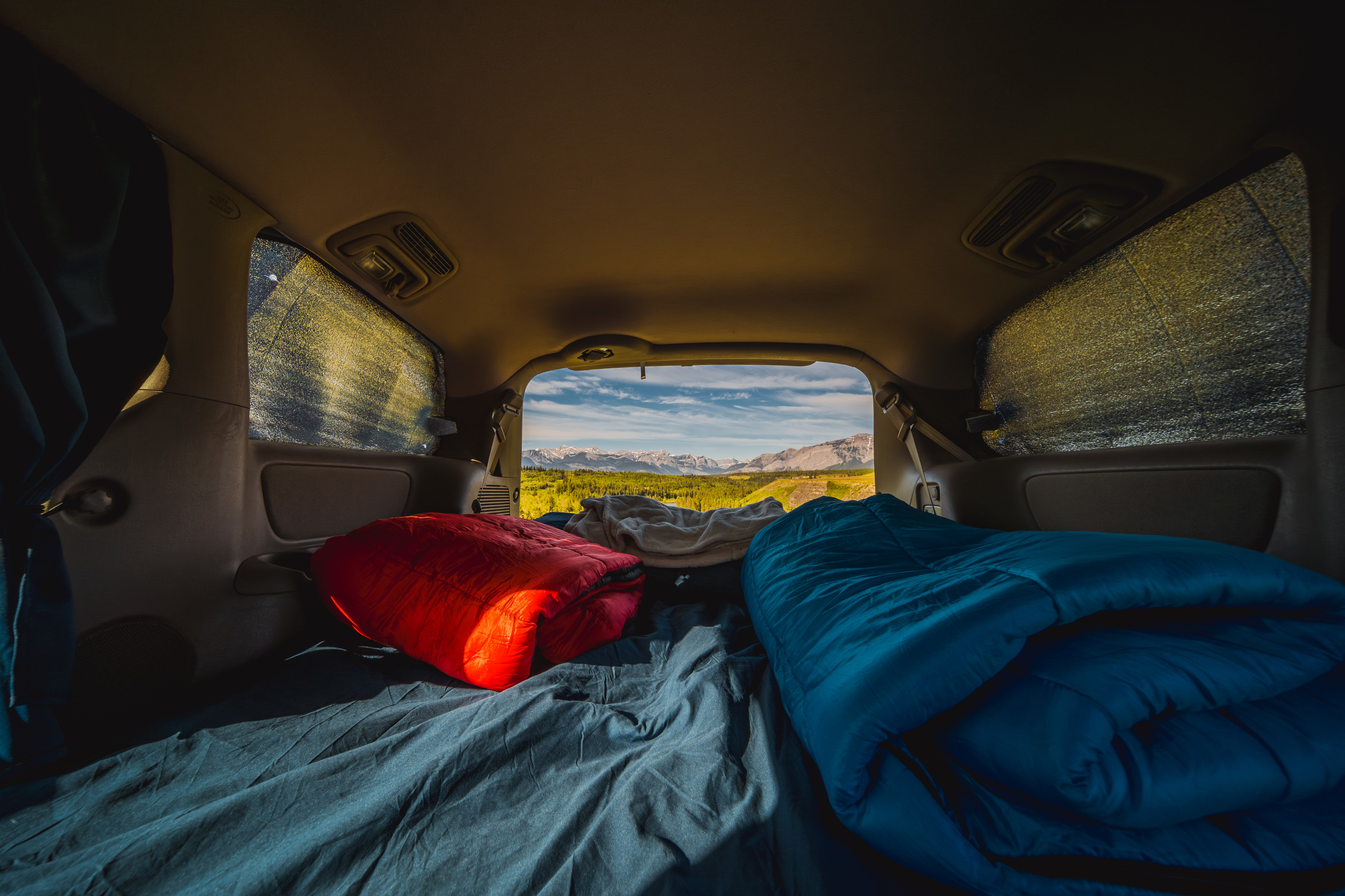 Cozy vehicle sleeping setup for adventure travel, with a scenic mountain view from the open rear of this RV rental.. Toyota Hiace campervan 2008