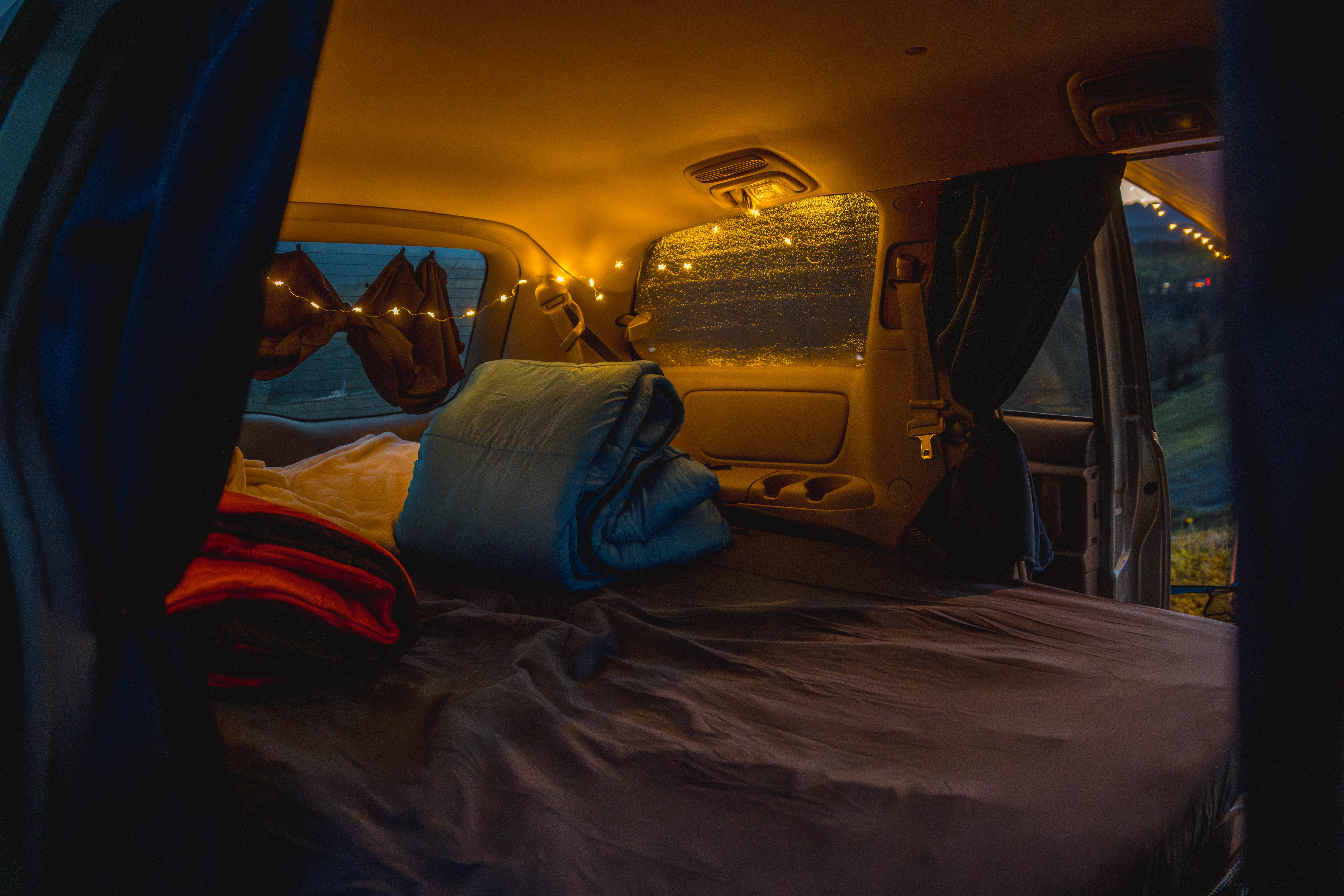 Cozy vehicle interior with a bed, fairy lights, and privacy curtains, perfect for an RV rental adventure.. Toyota Hiace campervan 2008