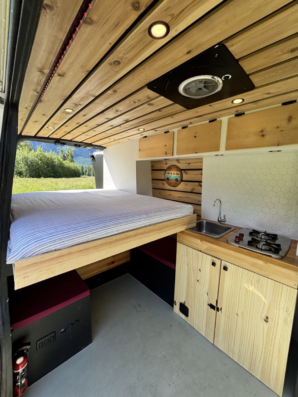 Modern RV rental conversion with wood ceiling, built-in bed, sink, stove, and overhead storage for comfortable travel.. Nissan PRIMASTAR 2019