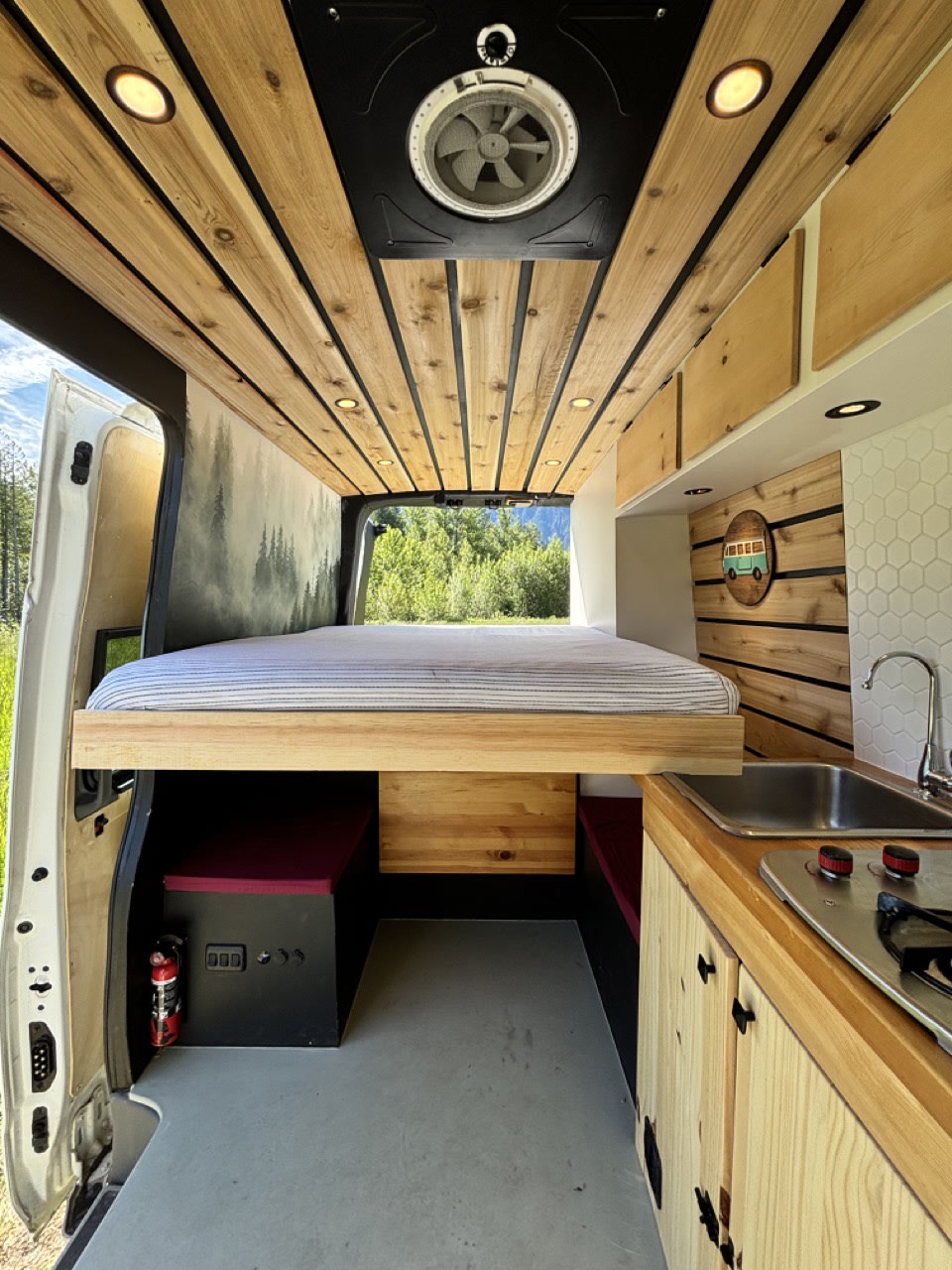 Cozy RV rental interior shows a compact living space: an elevated bed, wood-paneled ceiling, and functional kitchenette.. Nissan PRIMASTAR 2019