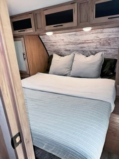 Step inside this cozy RV rental's bedroom, featuring a comfortable bed, wood-look headboard, and storage cabinets.. Forest River Cherokee 2024