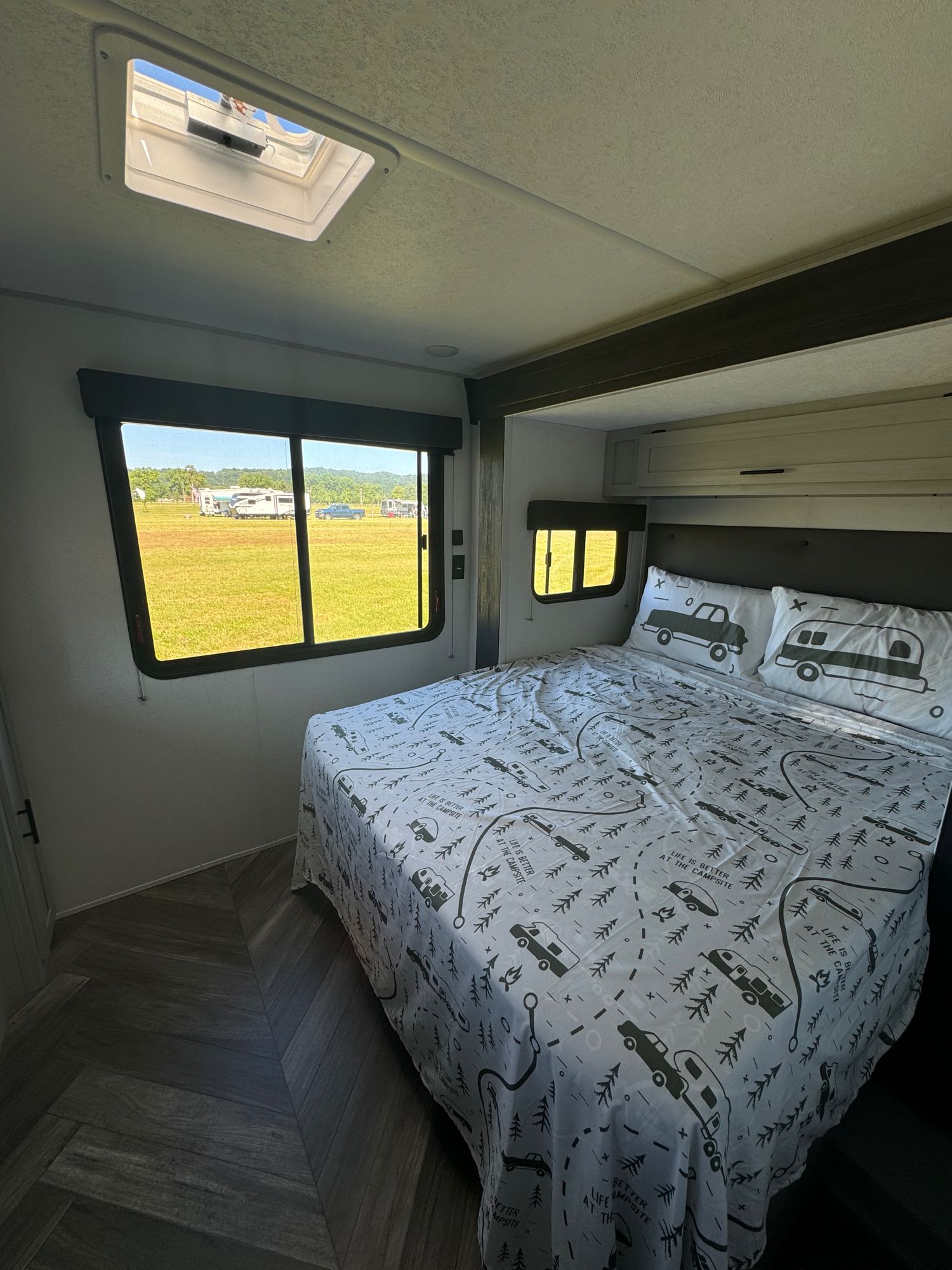 Cozy rv rental bedroom with camping-themed bedding, a large window view of an RV park, and an overhead skylight.. Forest River Wildwood FSX 2022