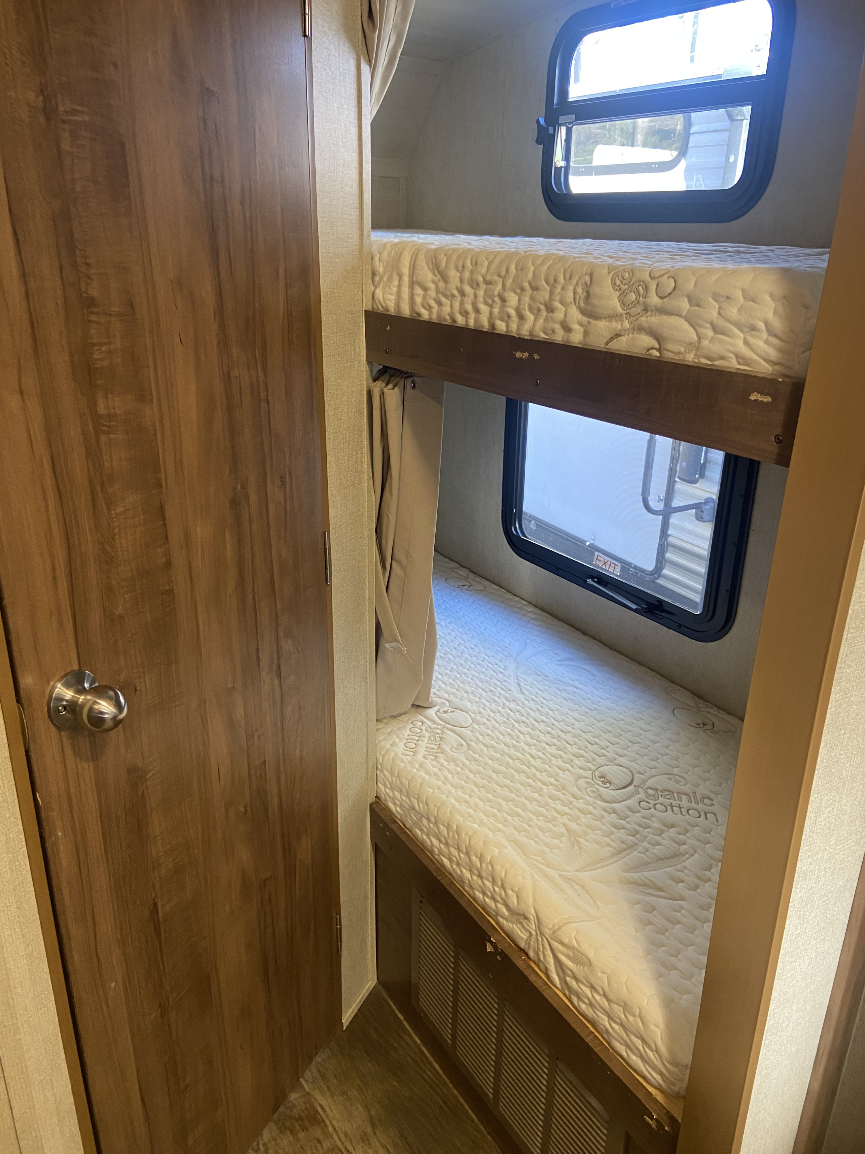 View inside an RV rental showing two stacked bunk beds with mattresses, windows, and a brown door. Cozy interior.. Gulf Stream Vintage Cruiser 2021