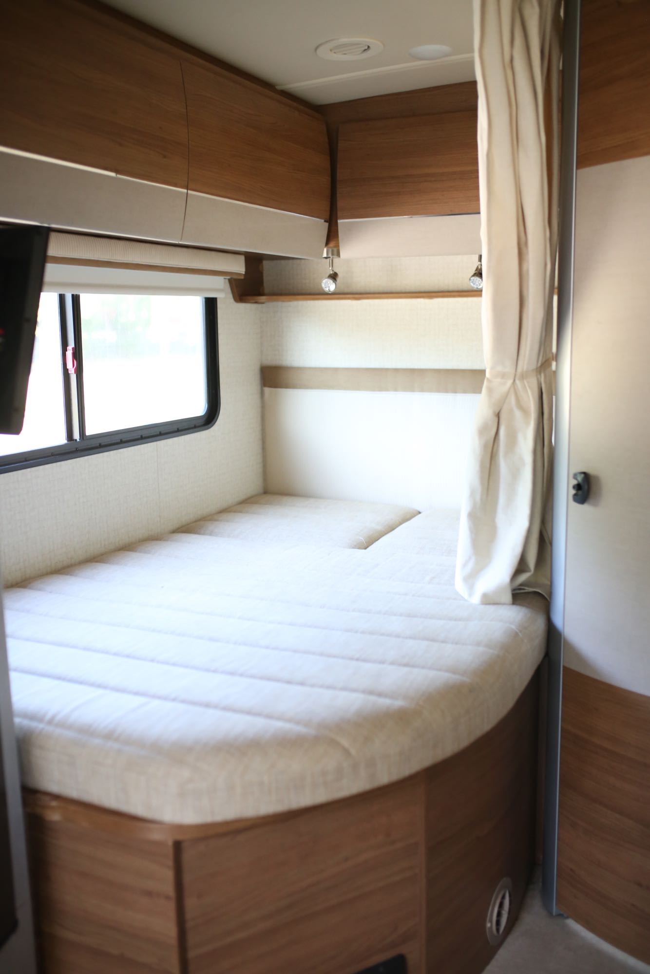 Cozy RV rental bedroom with a comfortable bed, overhead storage, and window, perfect for your next adventure.. Itasca Navion 2016