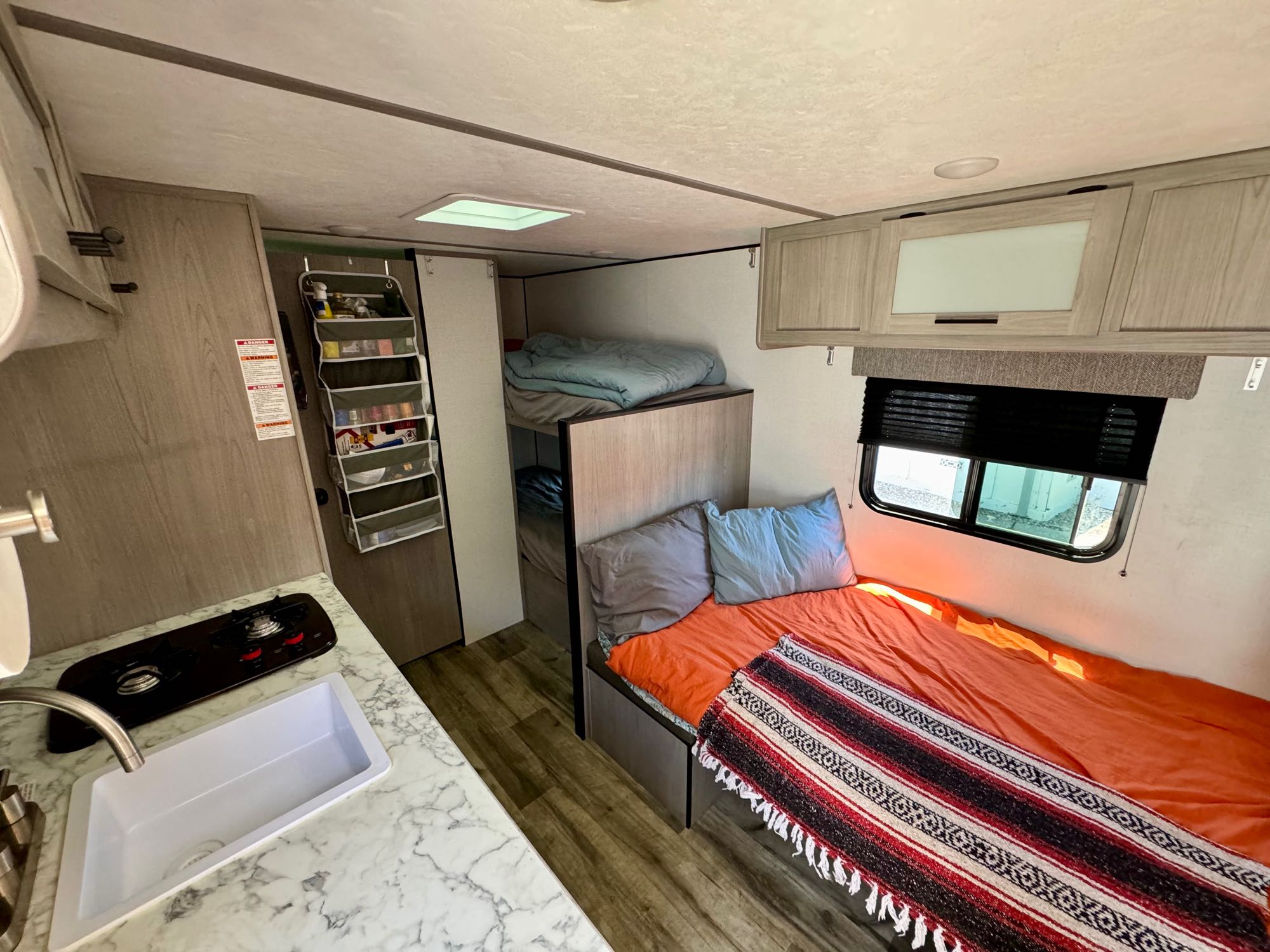 RV rental interior: A compact kitchen, bunk beds, and a comfortable main sleeping area with an orange blanket.. Coleman Lantern 17B 2024