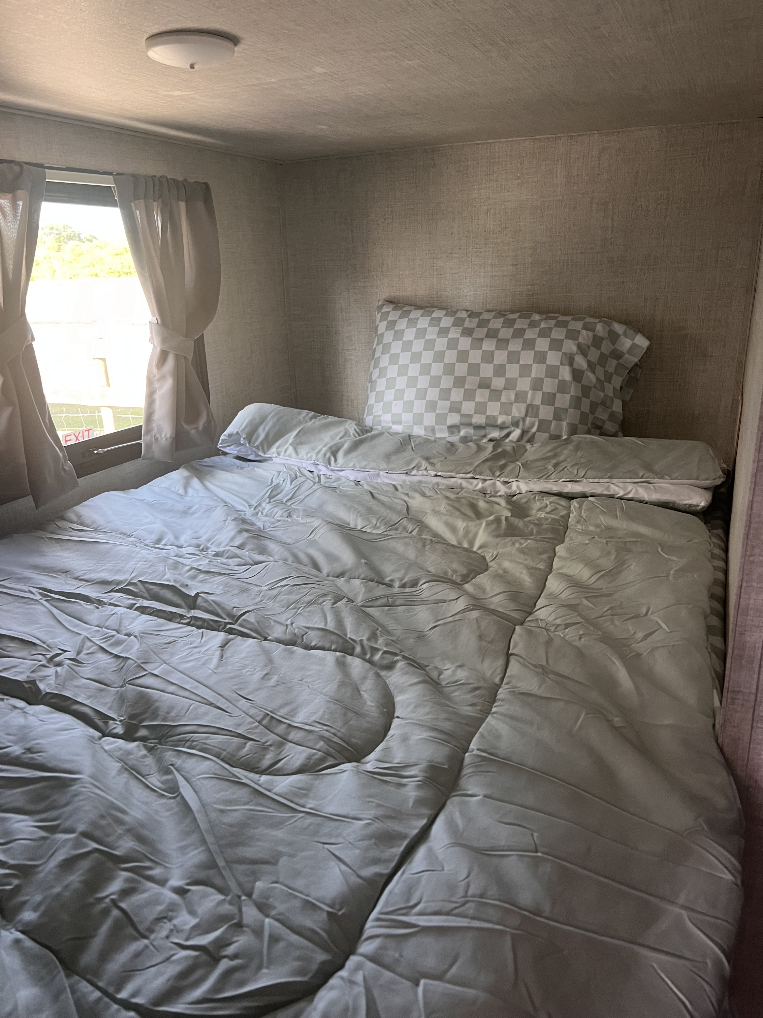Cozy RV rental bedroom showing a light-colored bed with a checkerboard pillow, window, and wall textures.. Gulf Stream Ameri-Lite 2022