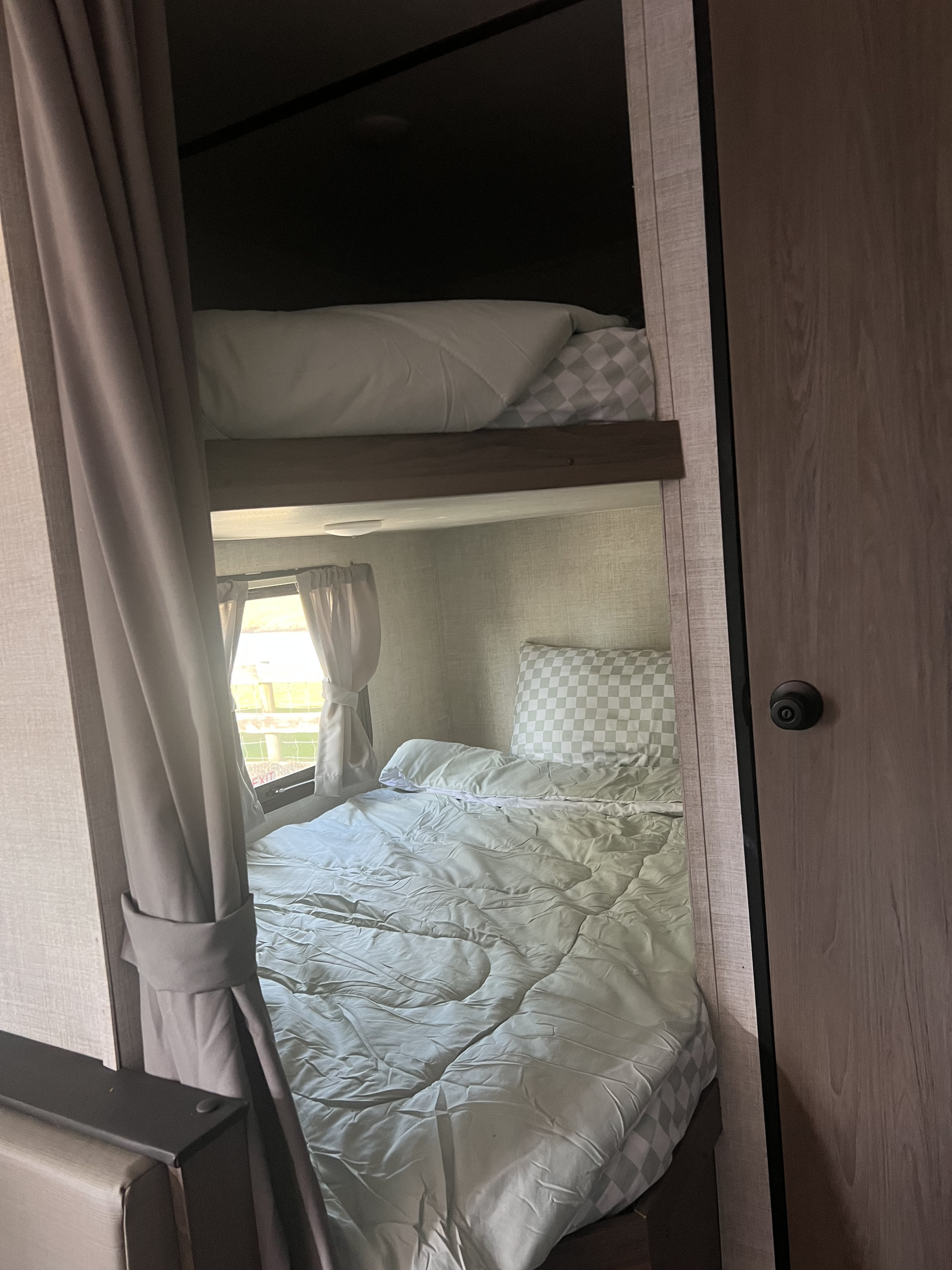 Inside an RV rental: comfortable bunk beds with checkered pillows, light bedding, and window curtains.. Gulf Stream Ameri-Lite 2022
