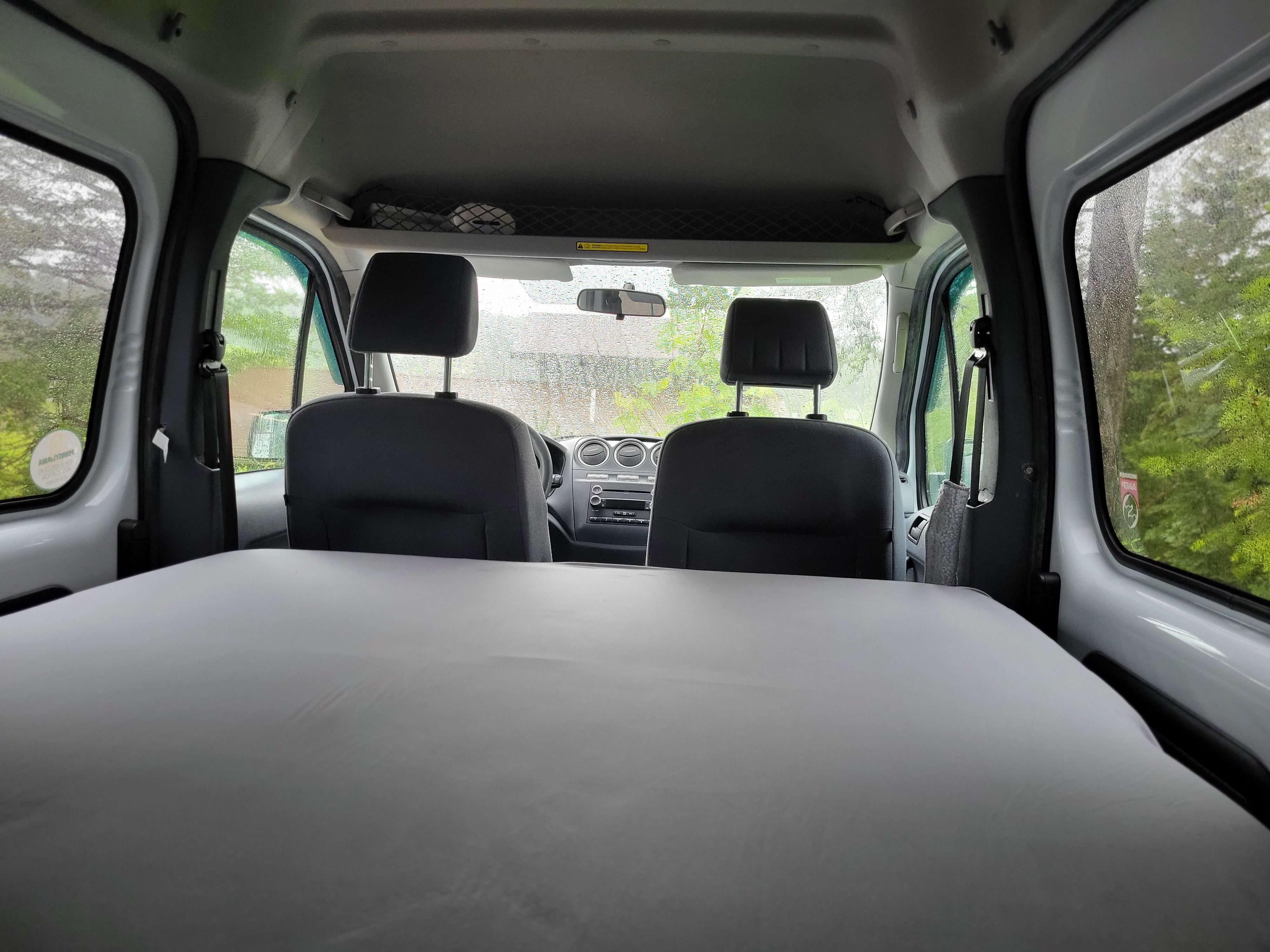 Interior of an RV rental, looking forward from the back over a grey sleeping platform to the front seats and dashboard.. Ford Transit 2013