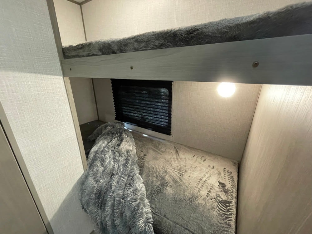 Inside an RV rental: a compact bunk bed setup with a window, reading light, and cozy blanket. Ideal for family travel.. Coleman latern lt 17b 2024