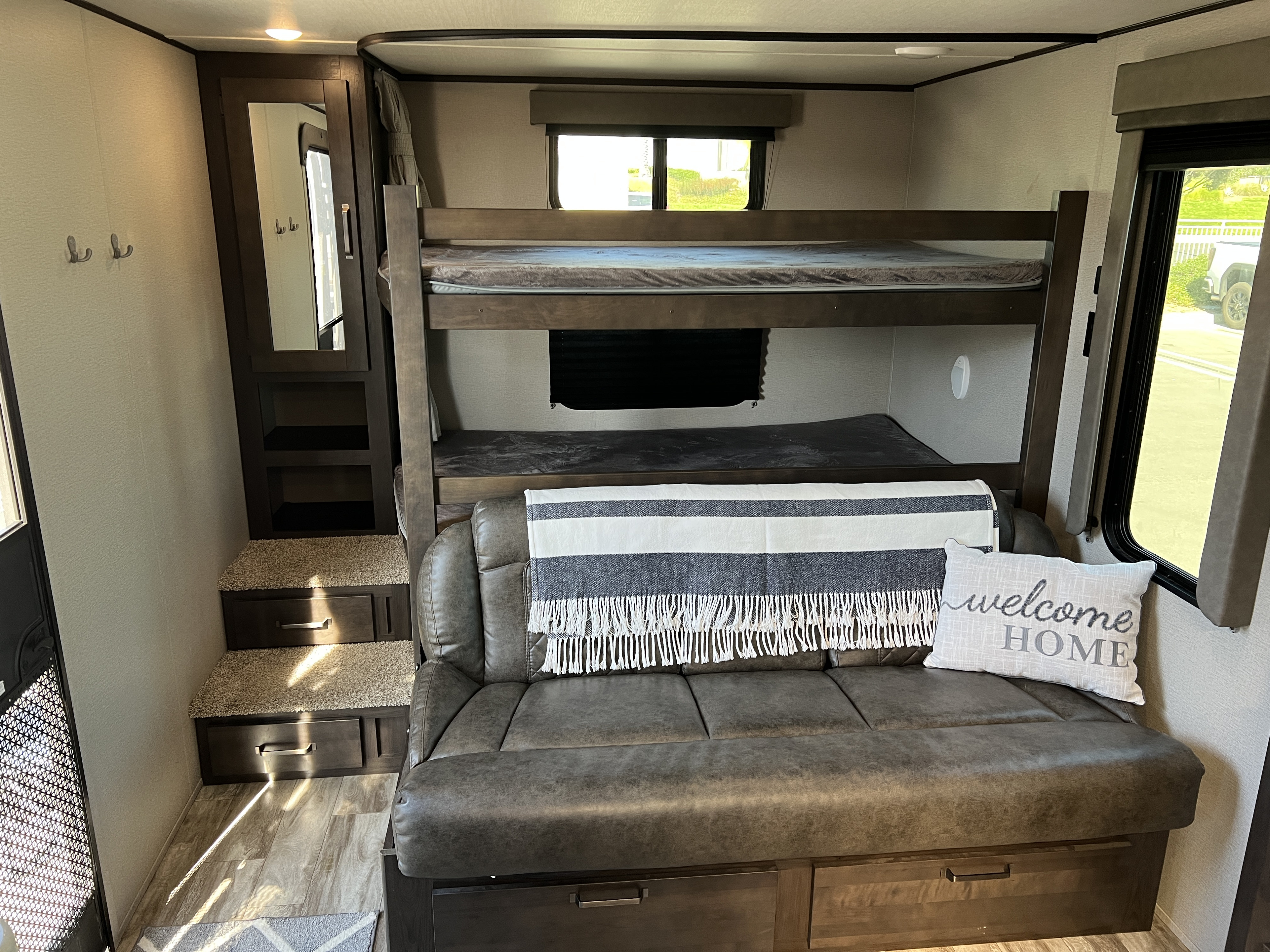 Cozy RV rental interior: bunk beds, convertible couch, mirror, and steps with storage. Ideal for family trips.. Grand Design Transcend Xplor 2021