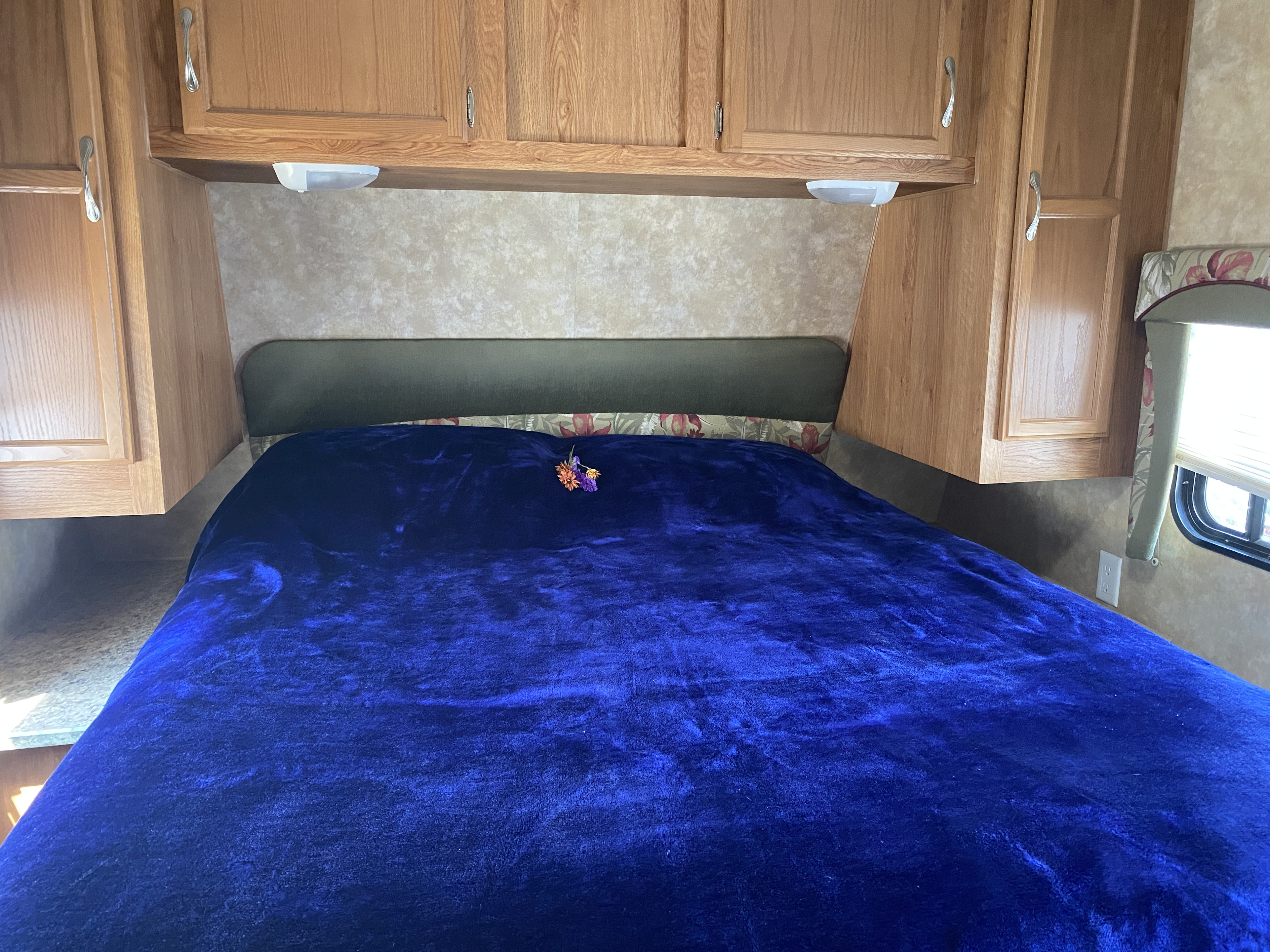 Cozy RV rental bedroom with a plush blue blanket, wood cabinets, and overhead lighting.. Jayco Jay Flight G2 2008