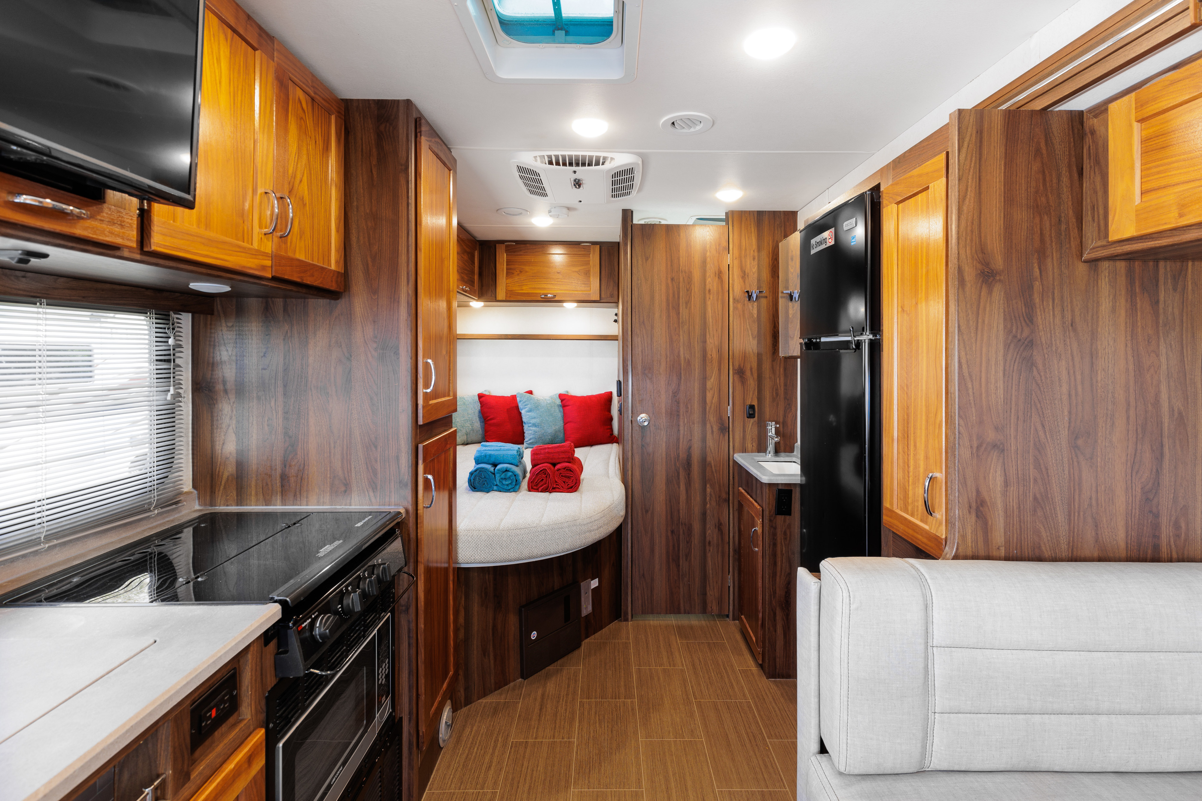 RV rental interior with a compact kitchen, comfortable bedroom featuring a round bed, and a living area, all with rich wood accents.. Winnebago VITA 2020