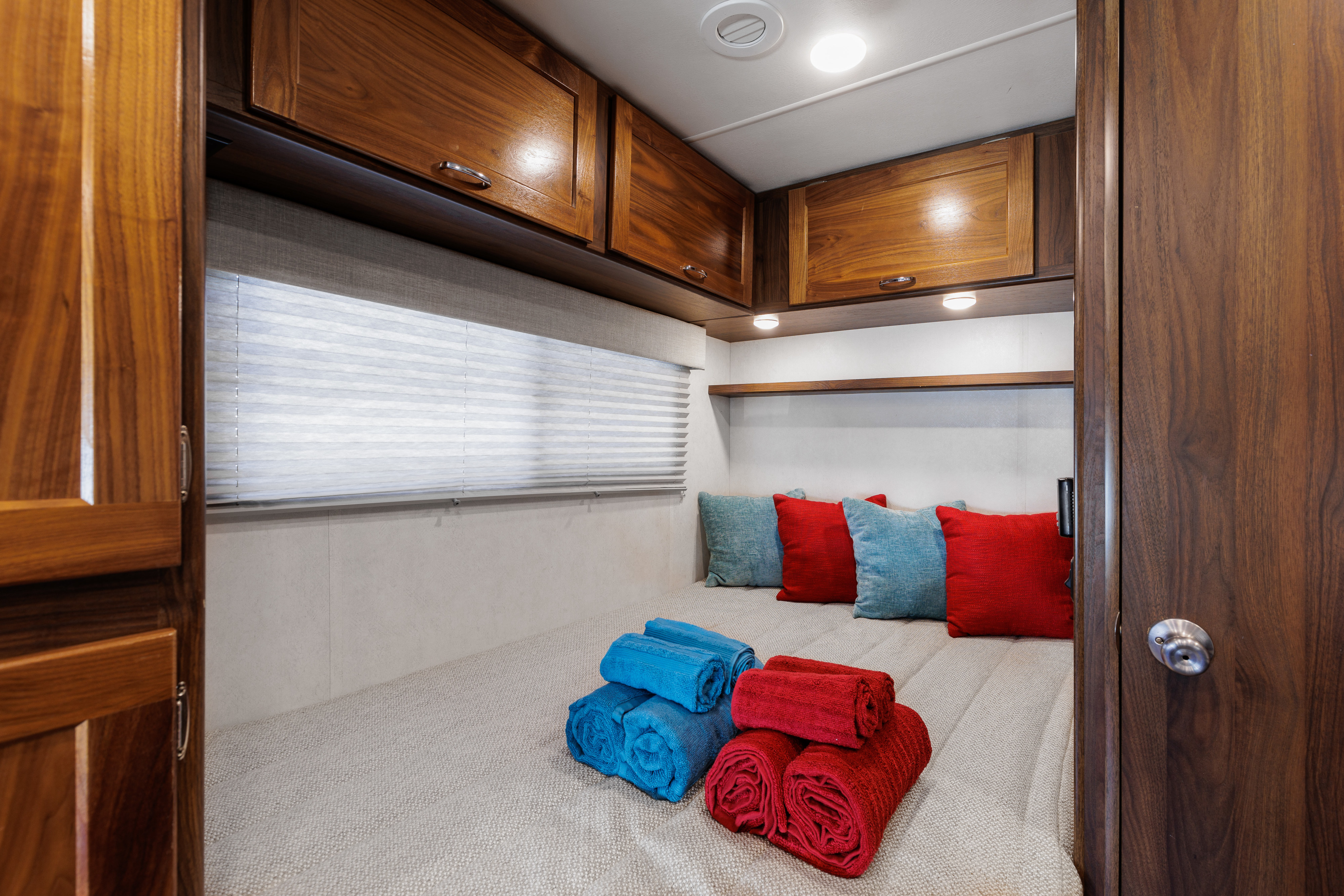 A comfortable RV rental bedroom interior, featuring a bed with colorful towels & pillows, and wooden overhead storage.. Winnebago VITA 2020
