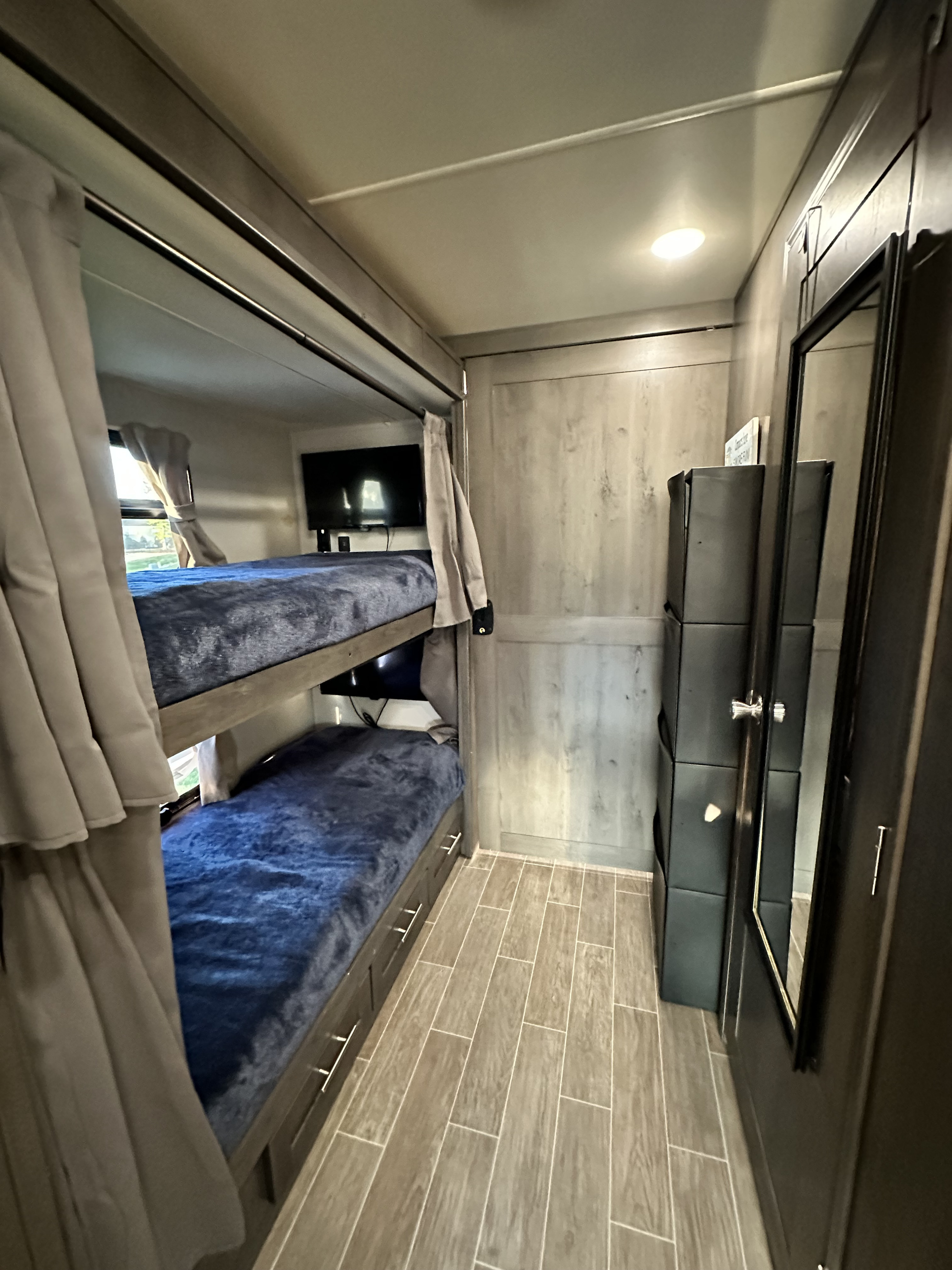 Inside an RV rental: cozy double bunk beds with blue blankets, mounted TV, convenient storage, and a full-length mirror.. Georgetown GT5 2021