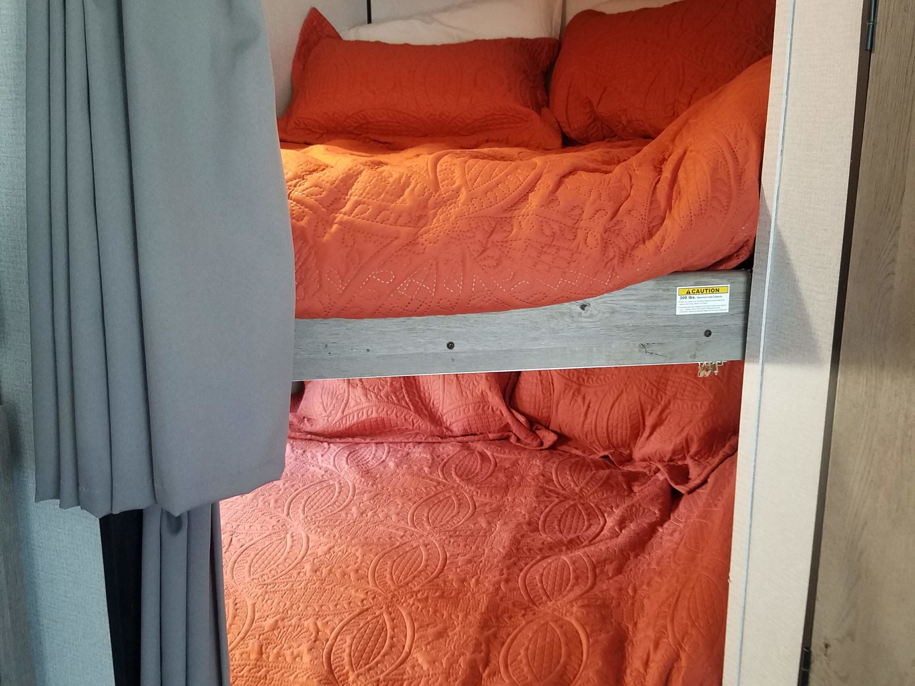 Cozy RV rental bunk beds: two bunks with orange quilted bedding, privacy curtains, and a top bunk safety beam (300 lb limit).. Keystone RV Springdale 2021