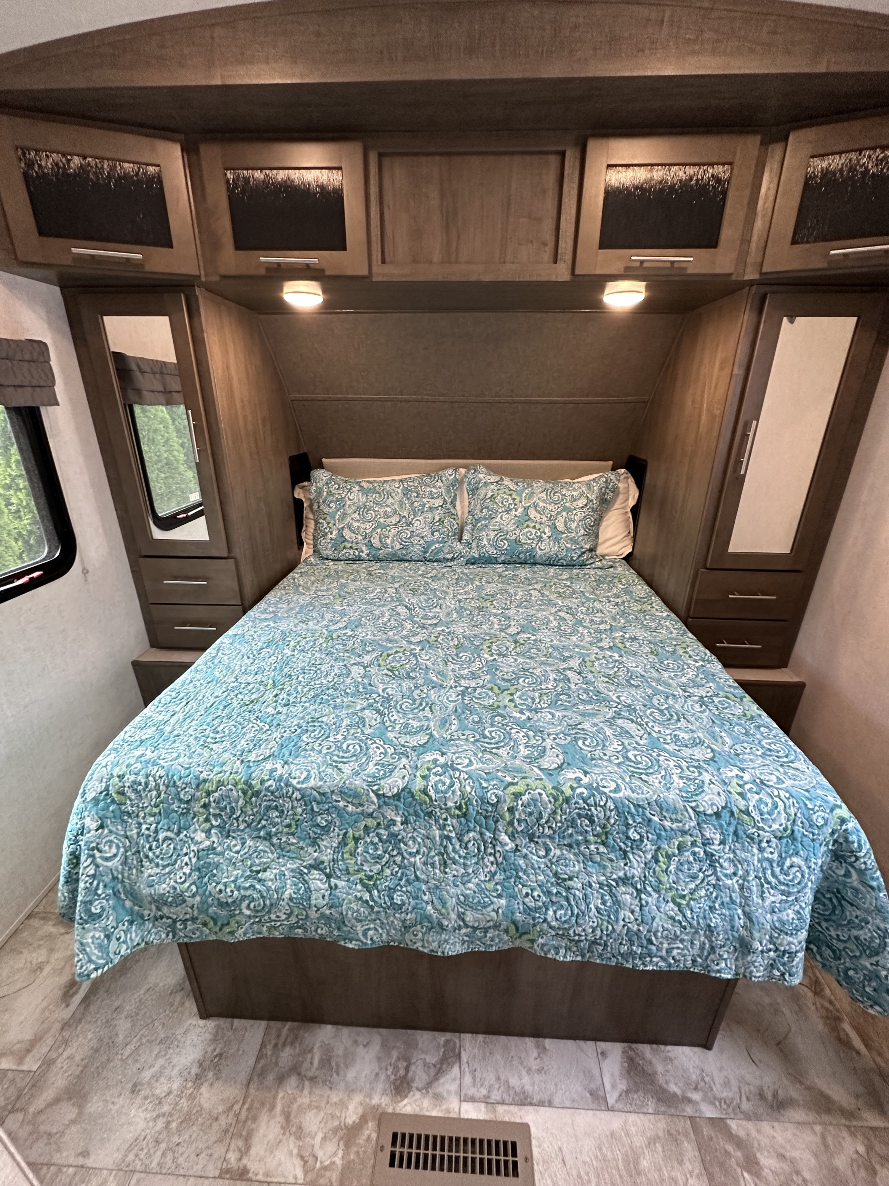 Bright RV rental bedroom showcasing a bed with blue patterned bedding, mirrored cabinets, and light wood-look flooring.. Forest River Surveyor 2018