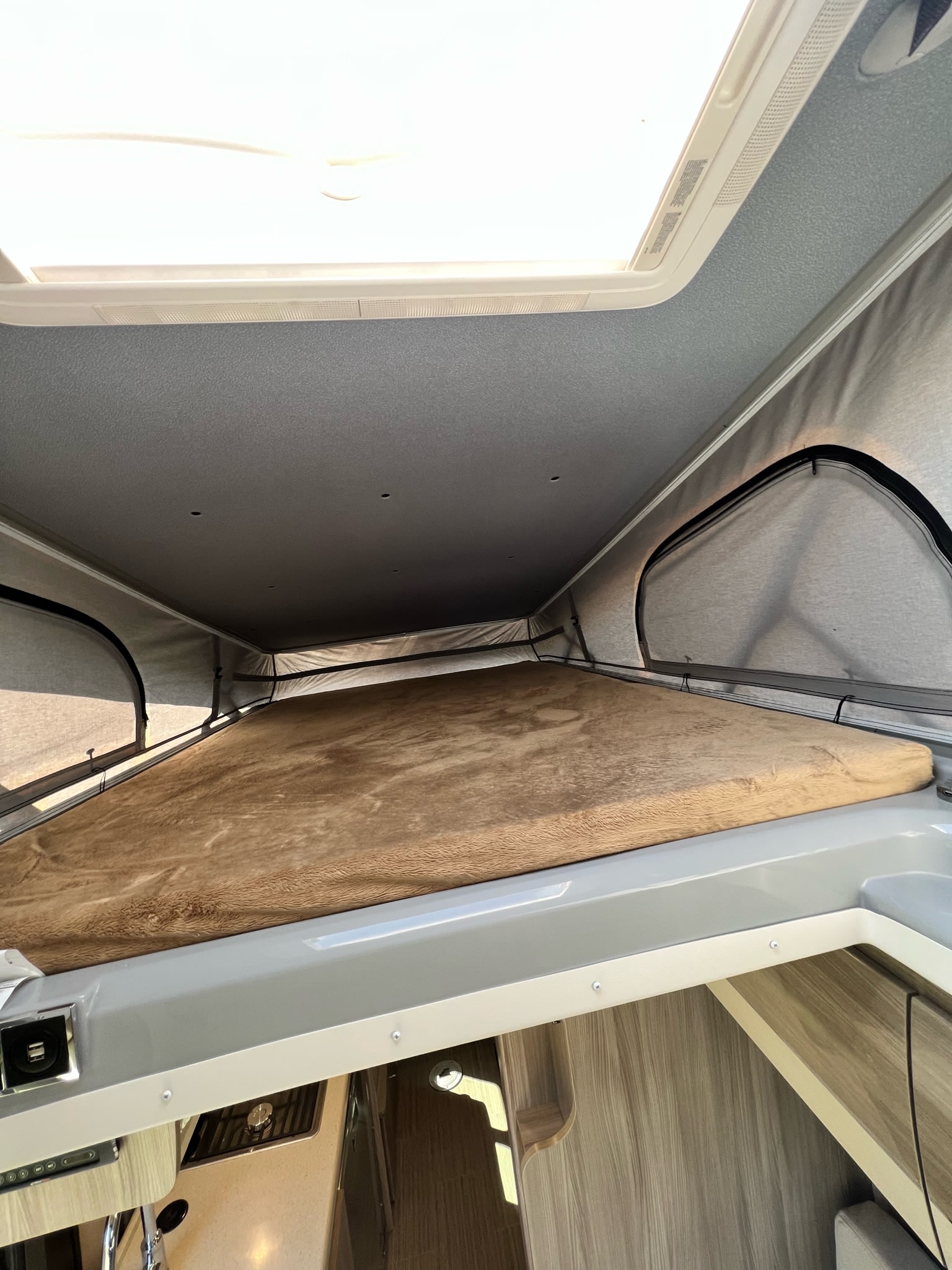 Spacious pop-top sleeping area in an RV rental, featuring a comfortable bed, skylight, and airy mesh windows.. Thor Sequence 2022