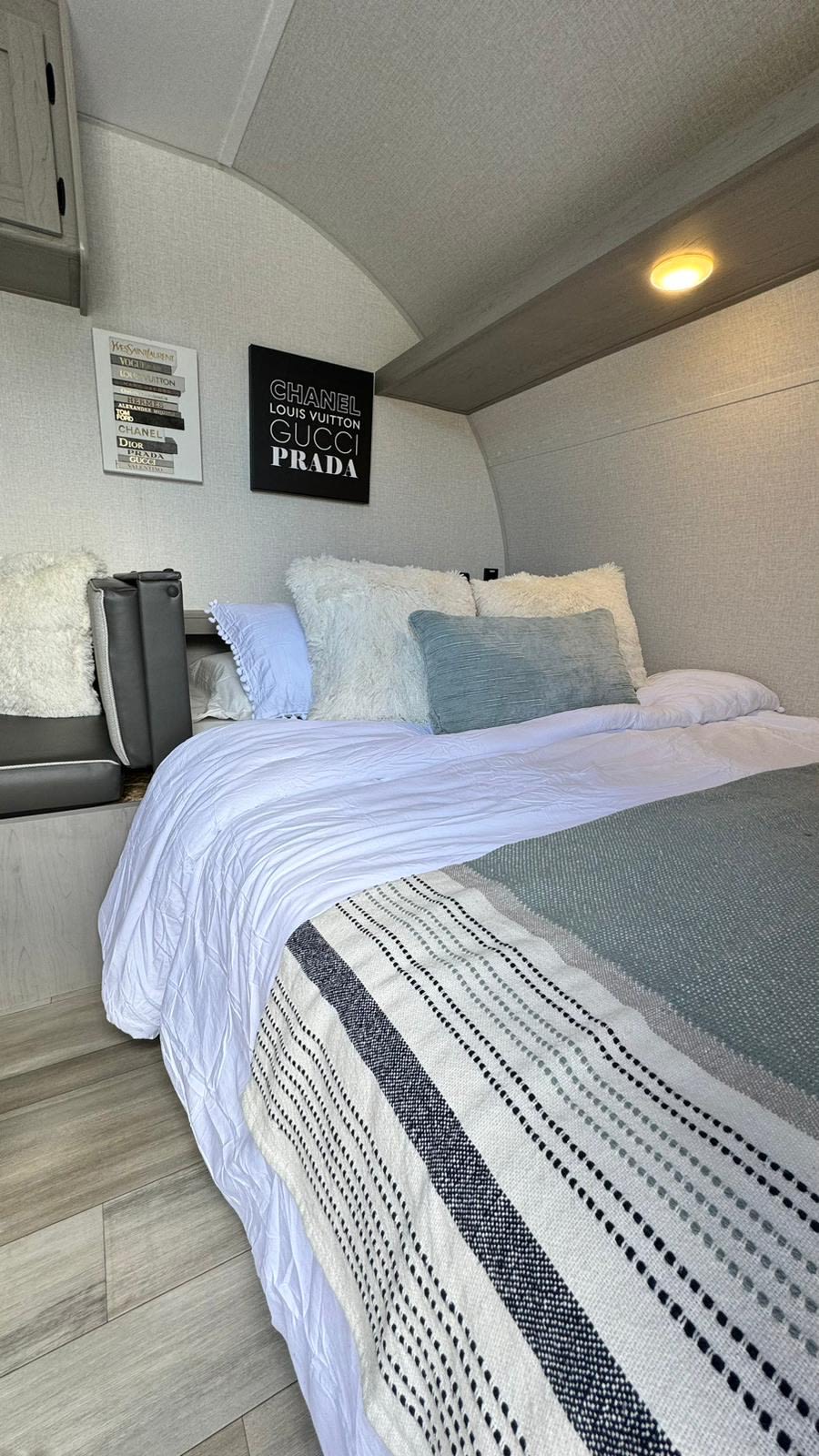 Modern RV rental bedroom setup: cozy bed with white linens & striped throw, decorative fashion art. Great for travel!. Forest River Viking 3K 2024