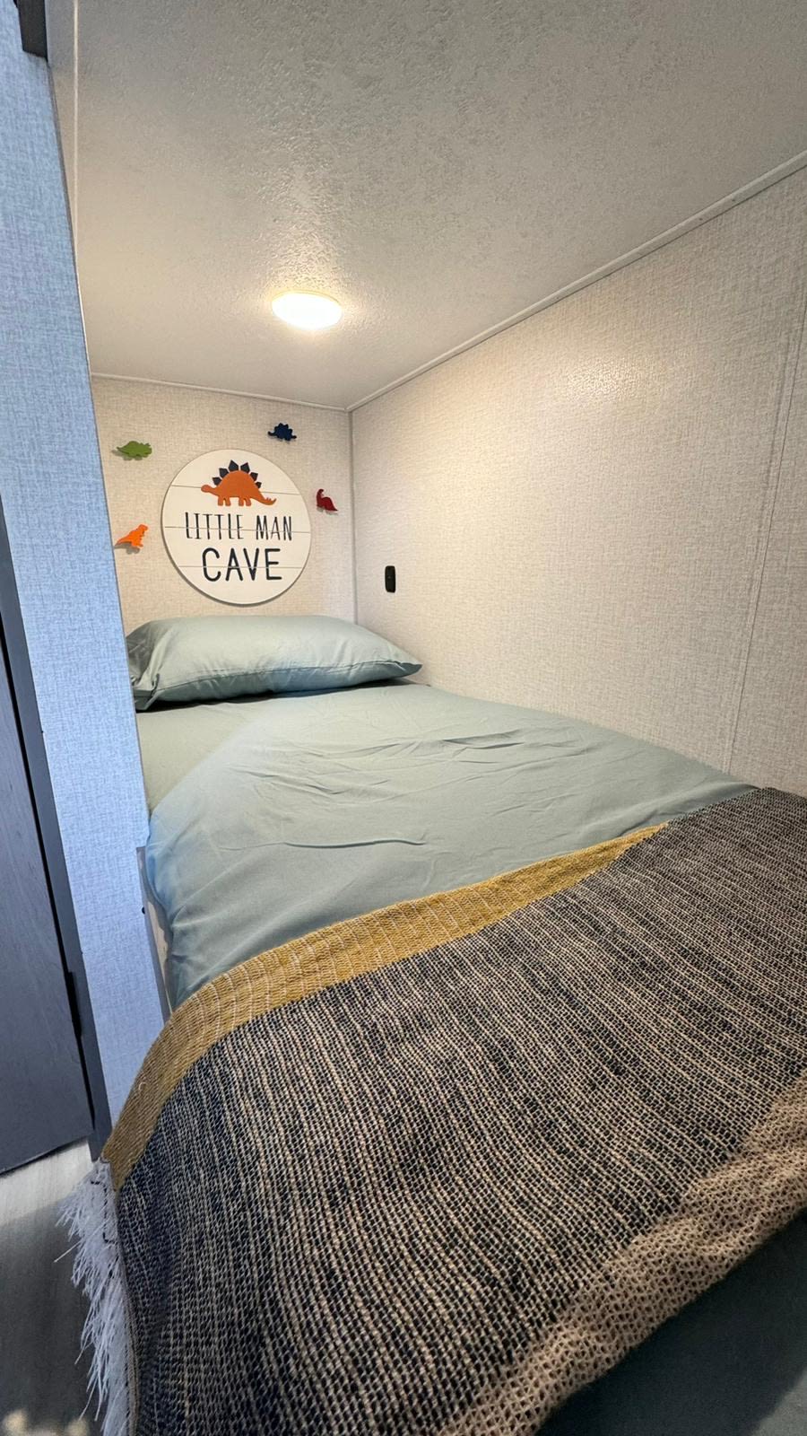 Inside an RV rental: a cozy child's bunk bedroom with light blue bedding, dinosaur decor, and a "Little Man Cave" sign.. Forest River Viking 3K 2024