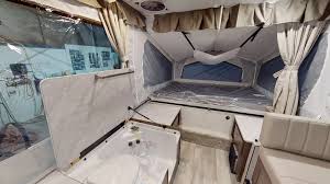 Inside a pop-up camper, perfect for an RV rental. Features a large bed & compact living area for camping.. Forest River Rockwood ESP 2019