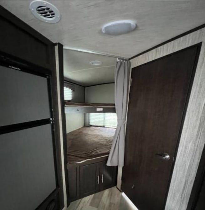 RV rental interior showing a sleeping area with bunk beds, a refrigerator, and an interior door.. Cruiser RV Fun Finder Xtreme Lite 2019