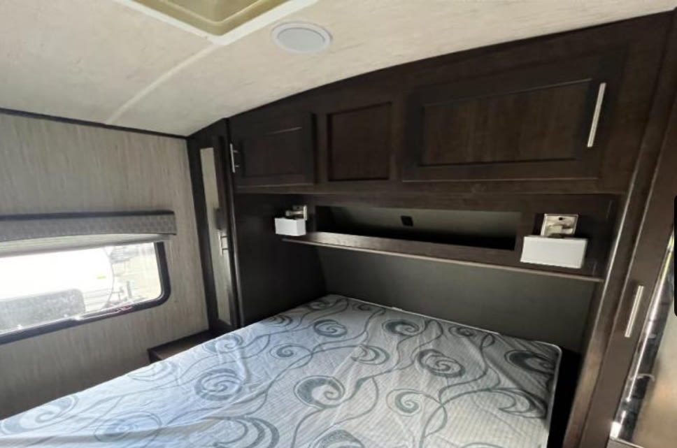 Spacious RV rental bedroom with dark wood cabinets, a patterned bed, and window.. Cruiser RV Fun Finder Xtreme Lite 2019