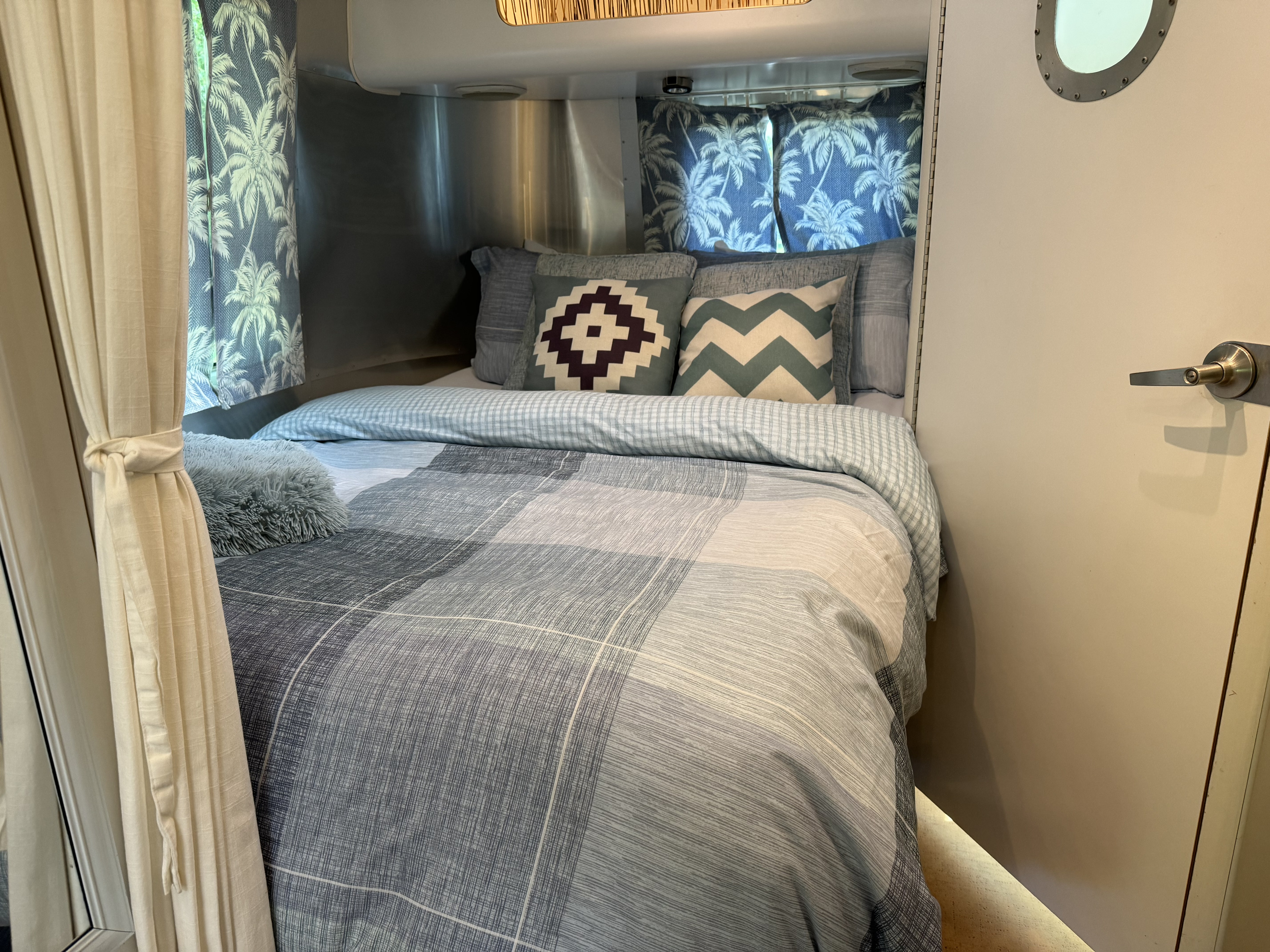 Cozy RV rental bedroom with blue plaid bedding, decorative pillows, tropical curtains, and sleek metallic walls.. Airstream International 2007