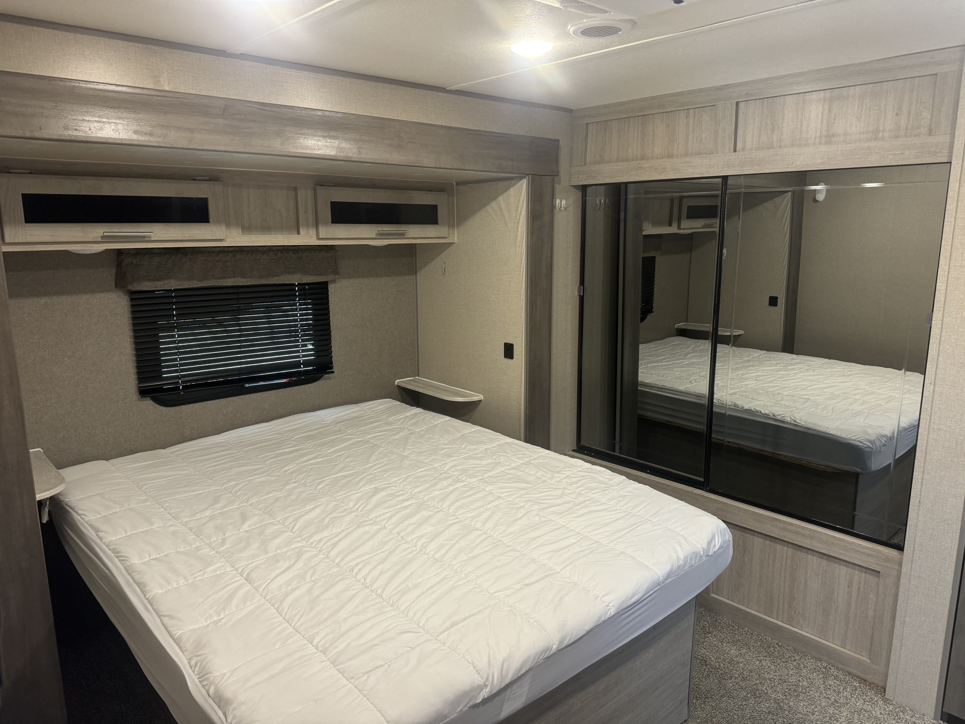 Inside this RV rental, discover a cozy bedroom featuring a comfortable bed, overhead cabinets, and a mirrored wardrobe.. Forest River Catalina 2022