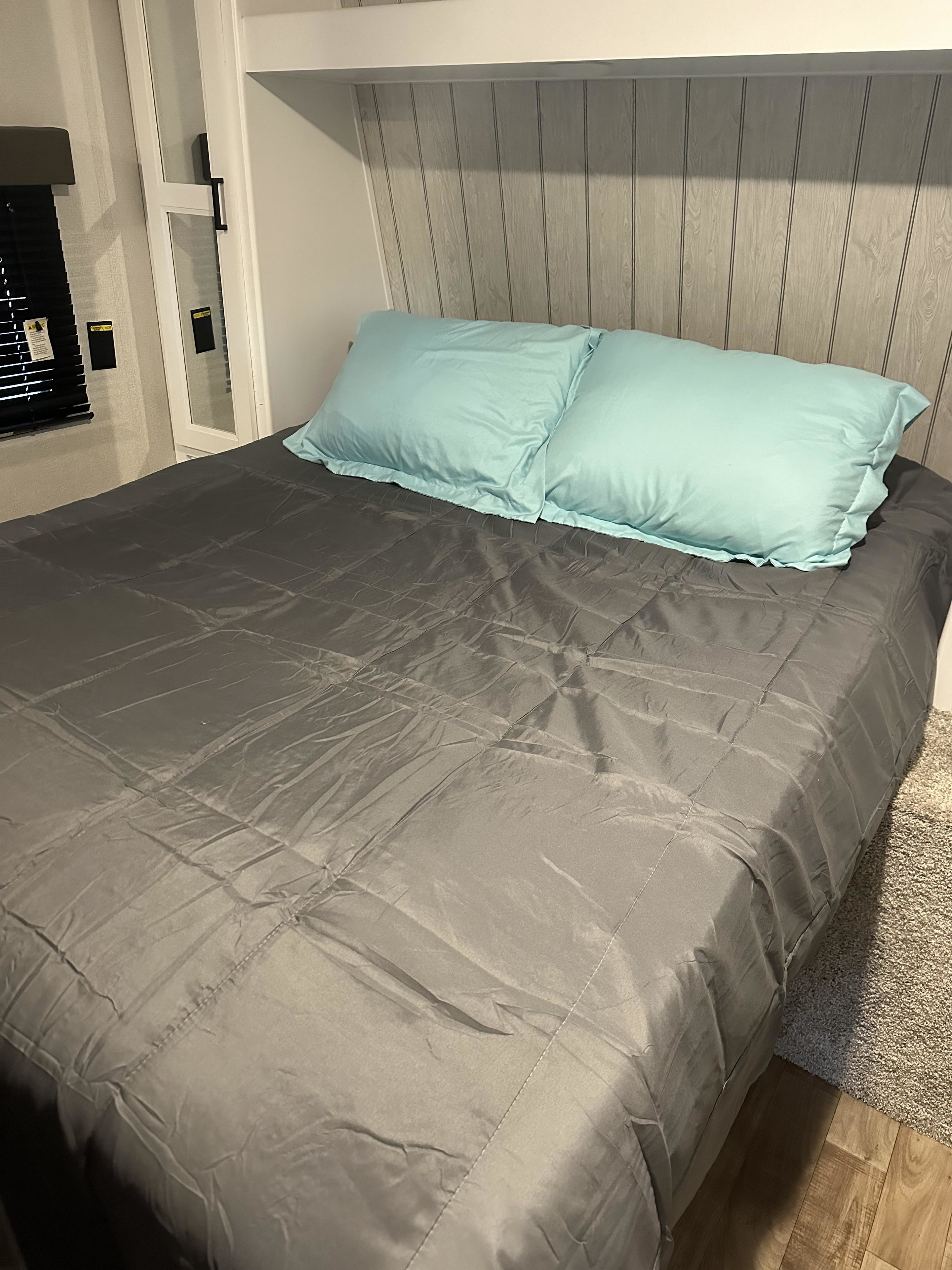 Comfortable RV rental bedroom with a neatly made grey bed, light blue pillows, and wood-panel headboard, ensuring a restful stay.. Keystone Hideout 2022