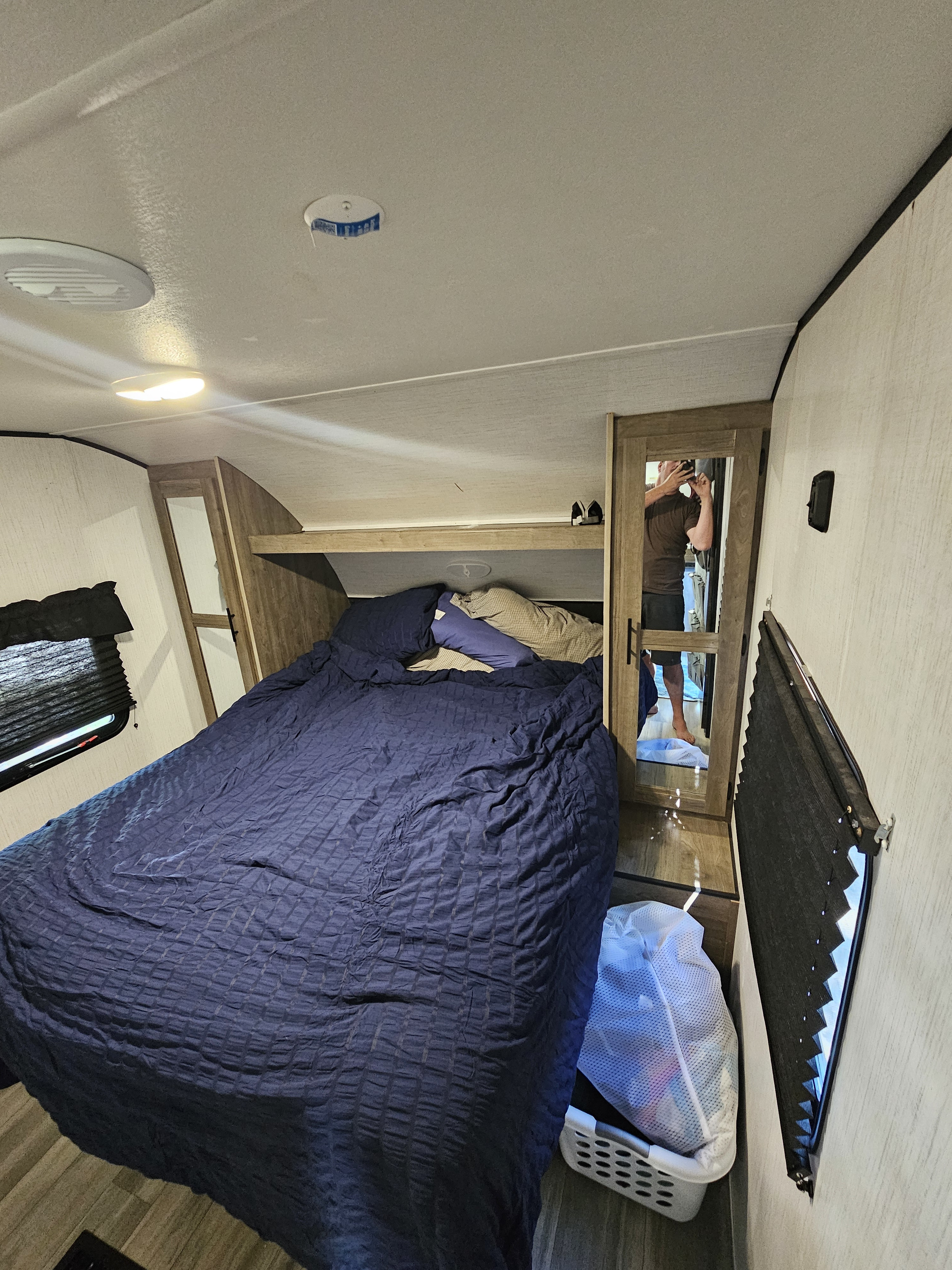 Compact RV rental bedroom with blue bed, mirrored closet, and window.. Heartland RVs Pioneer 2022