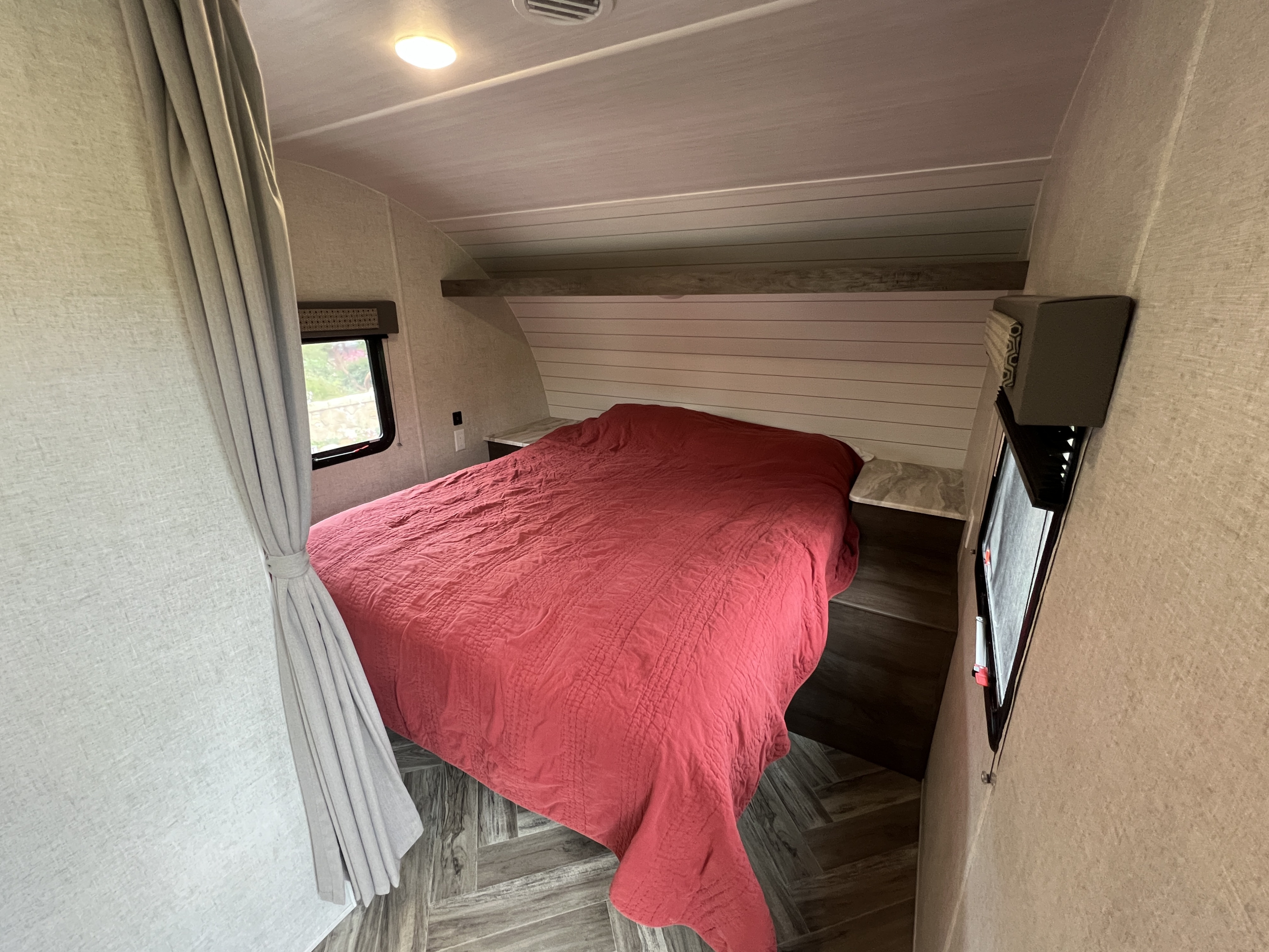 This cozy RV rental features a comfortable bedroom with a red quilted bed, built-in nightstands, and a window.. Forest River EVO 208RD 2021
