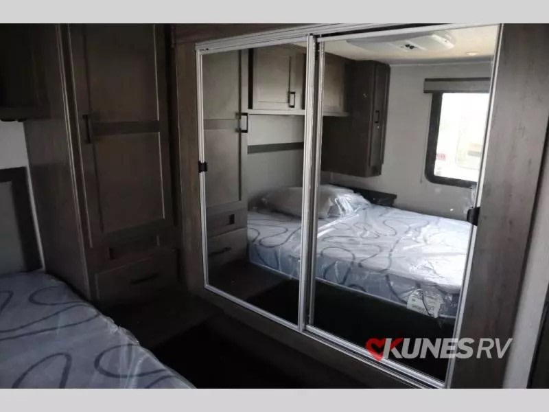 Compact RV rental bedroom with mirrored closet, two beds (one covered), and dark wood storage cabinetry.. Coachmen Leprechaun 2024