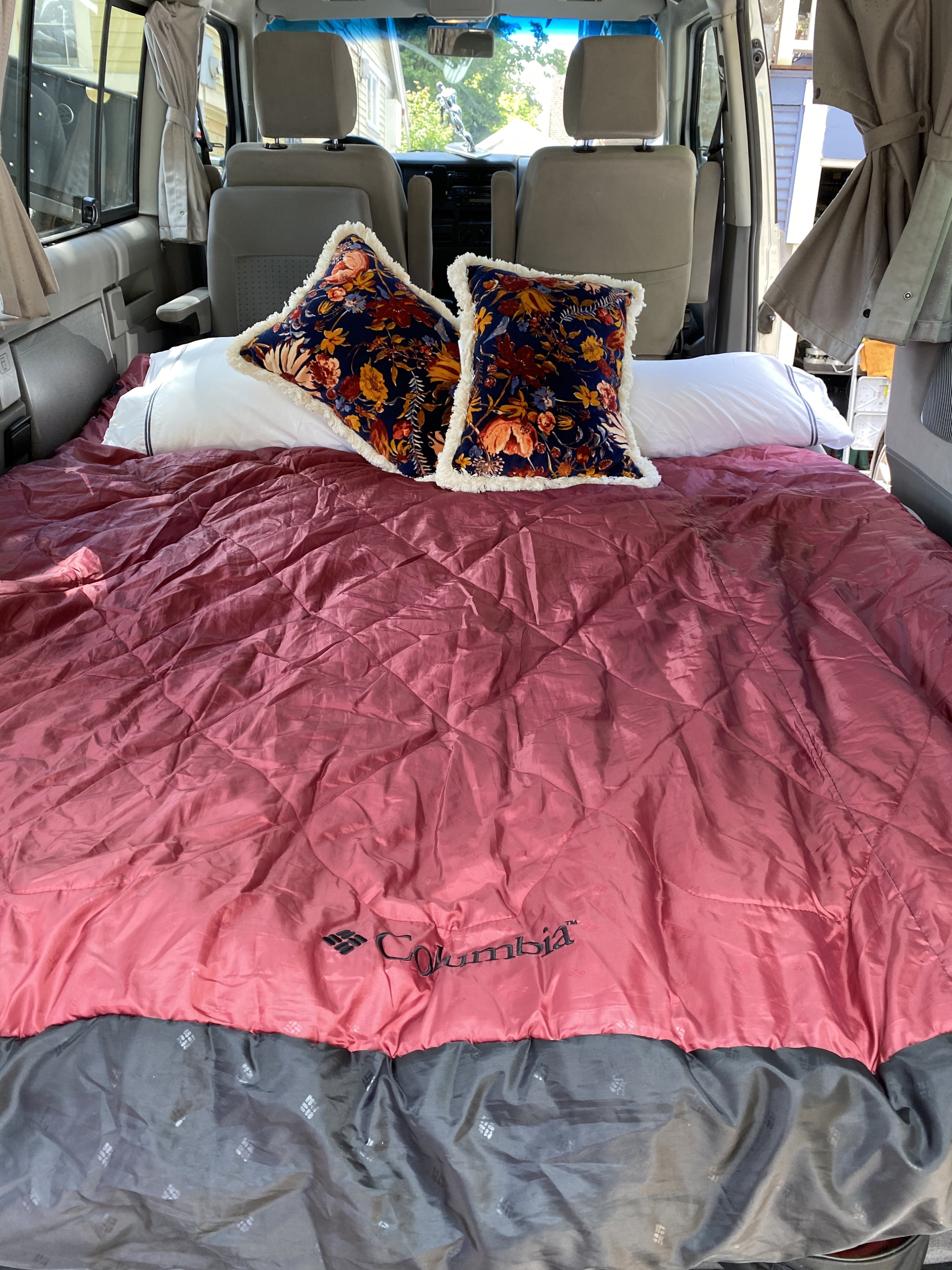 Cozy RV rental sleeping setup inside a van. Features a bed with white pillows and a quilted pink Columbia blanket.. Volkswagen Westfalia 2003