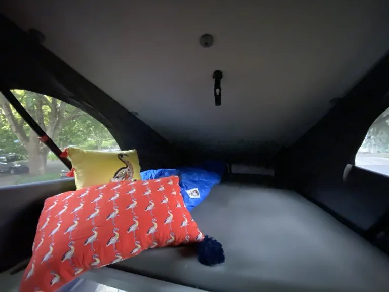 Cozy RV rental pop-top camper interior. A bed with grey mattress, yellow & red bird-patterned pillows, and a blue sleeping bag.. Volkswagen Westfalia 2003
