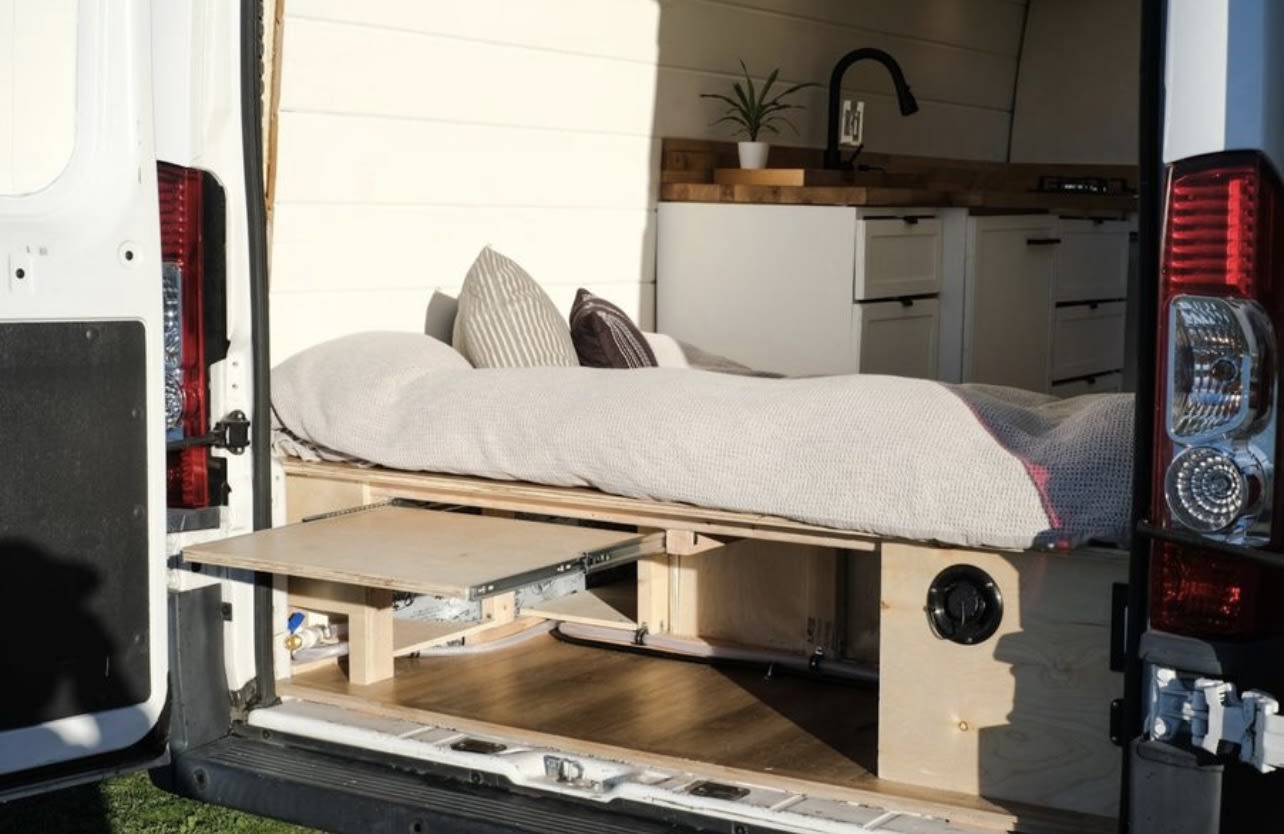 View from the rear of a cozy rv rental campervan showing a comfortable bed, pull-out table, and compact kitchen.. Dodge Ram 1500 2015